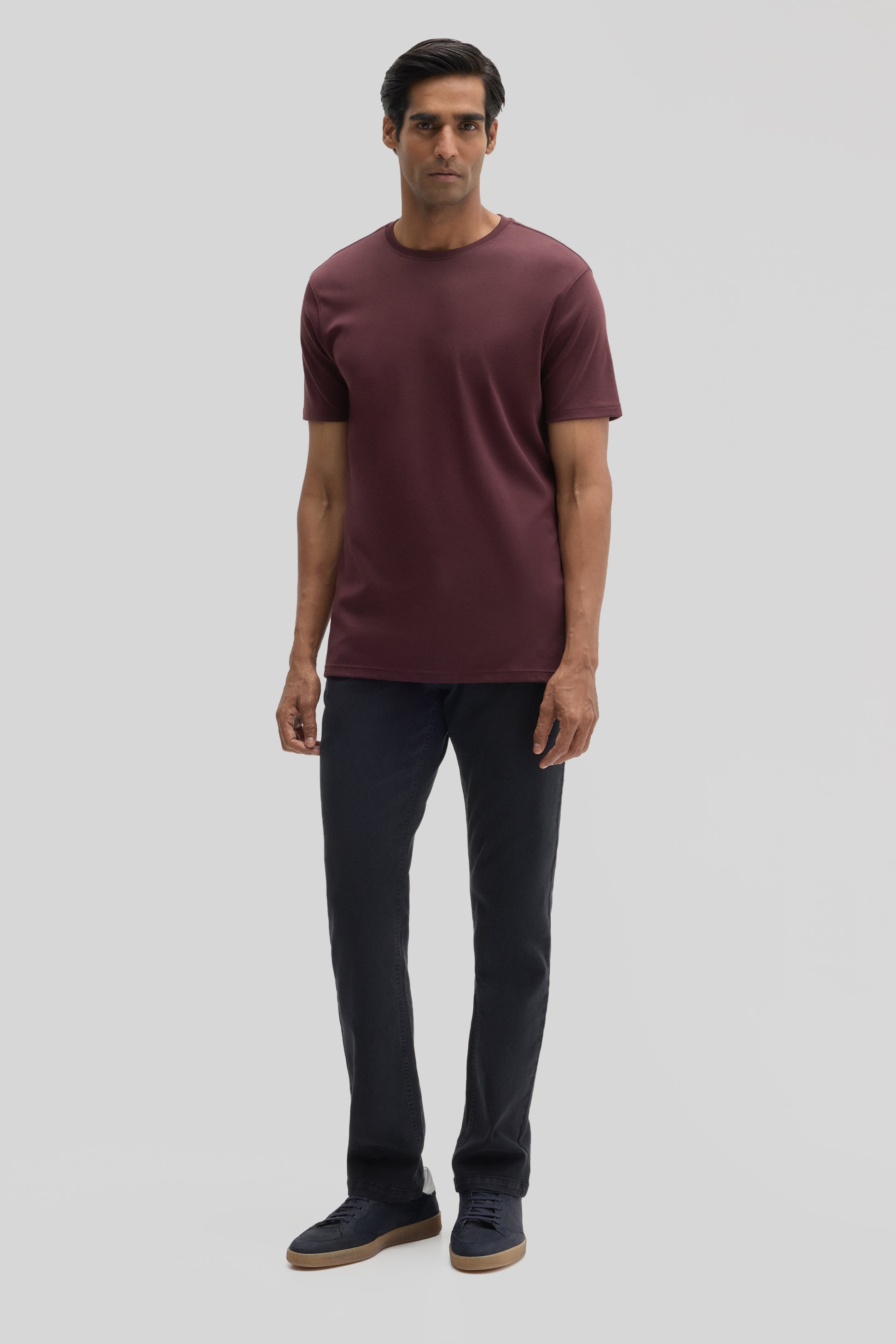 Man wearing burgundy crew neck t-shirt with short sleeves and dark navy pants.