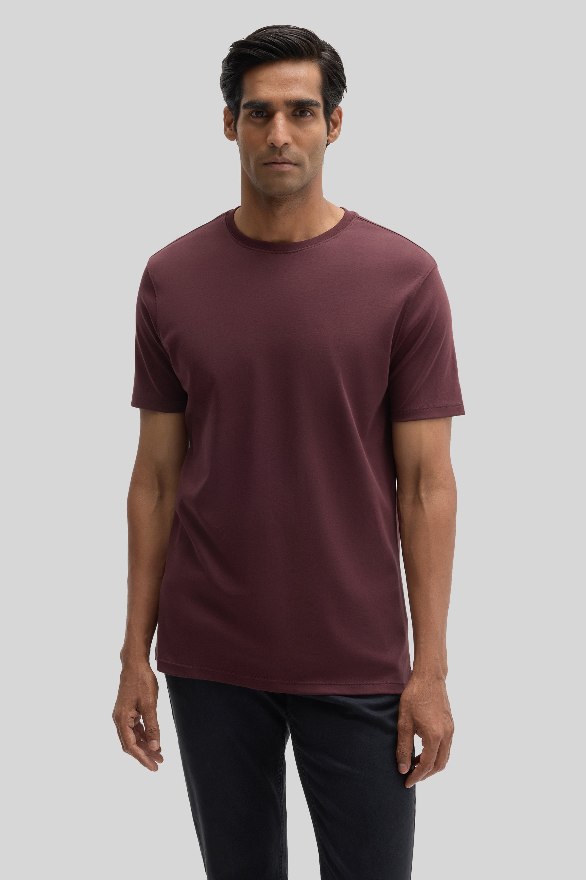 Man wearing a burgundy short-sleeved crew neck t-shirt with black pants.