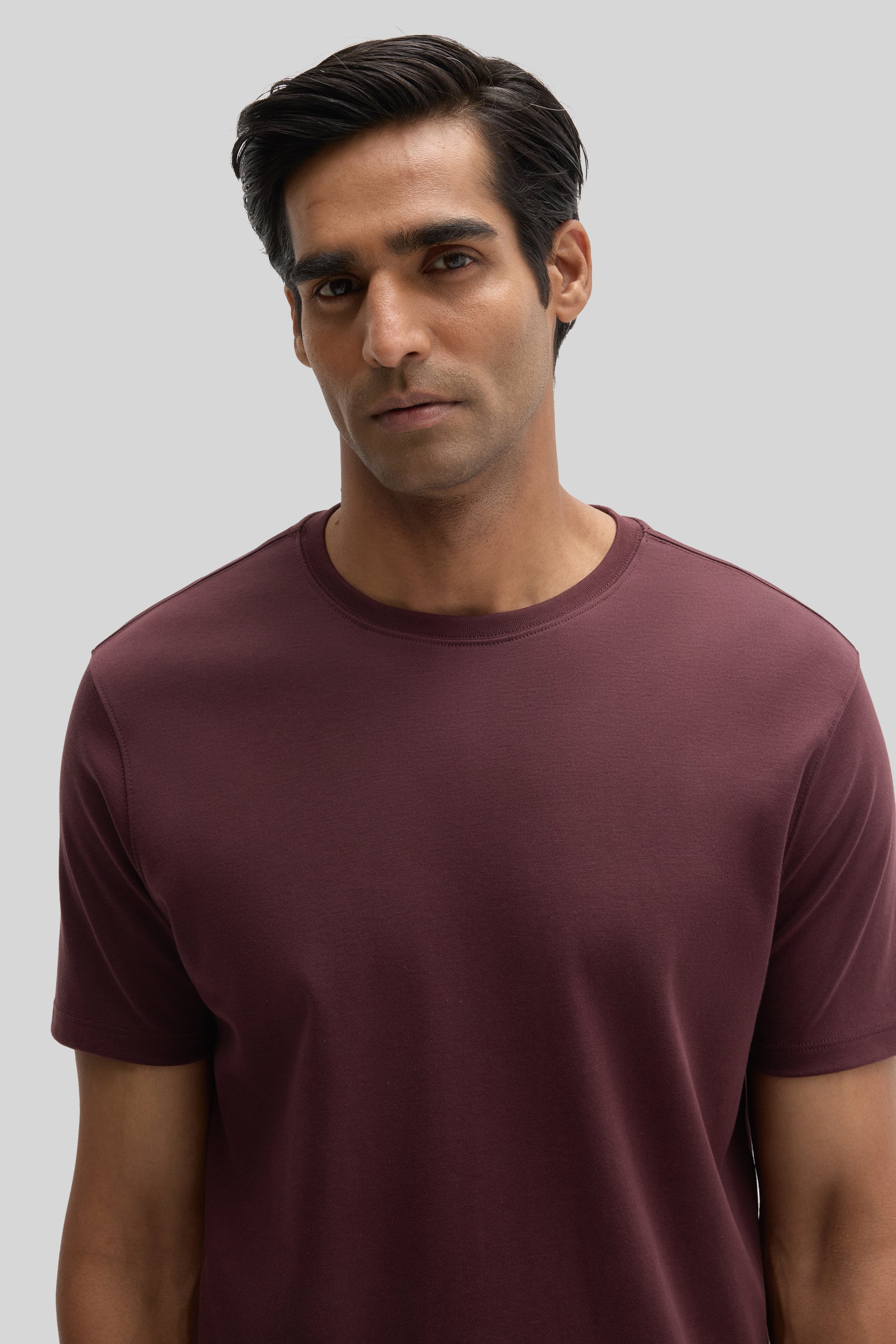 Man wearing burgundy crew neck short-sleeve t-shirt against neutral background.