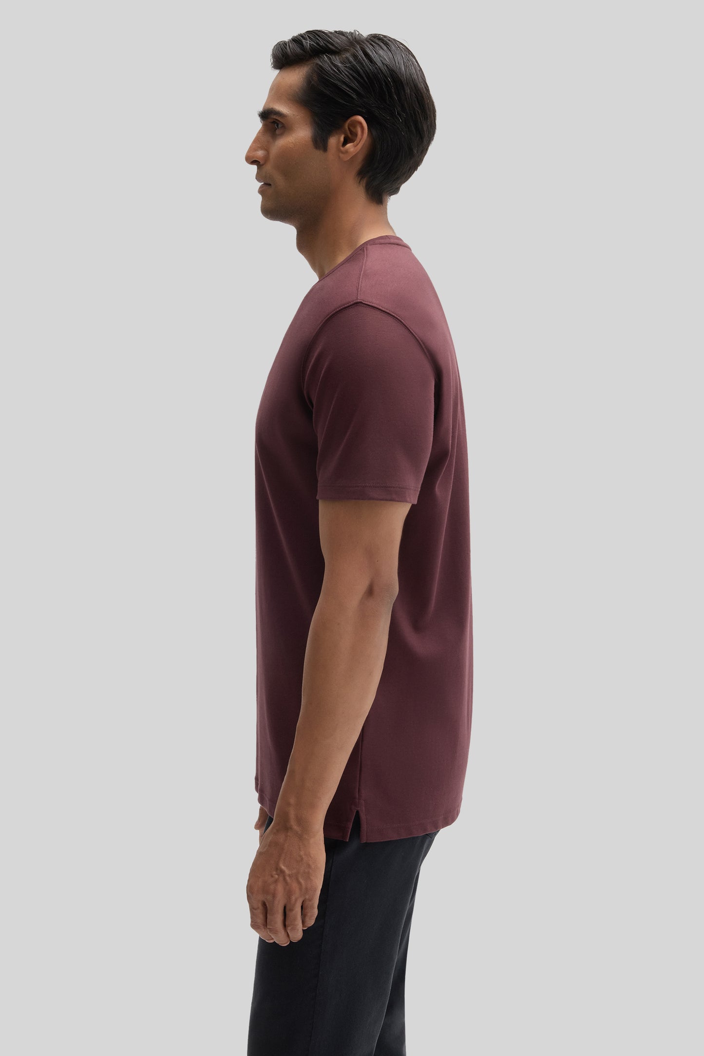 Man wearing a burgundy short-sleeve t-shirt with black pants, shown in profile view.
