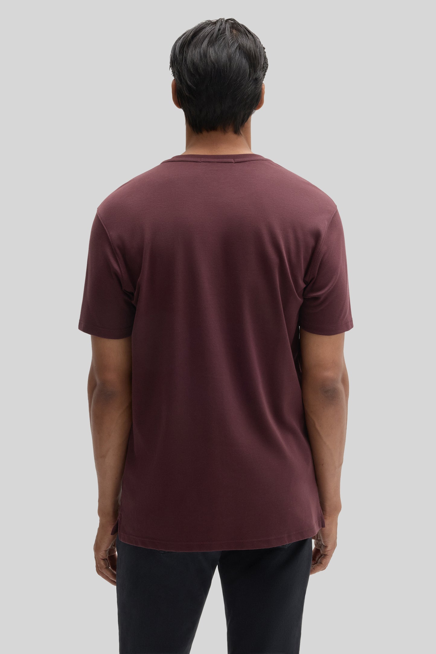 Burgundy crew neck t-shirt with short sleeves shown from back view on male model wearing black pants.