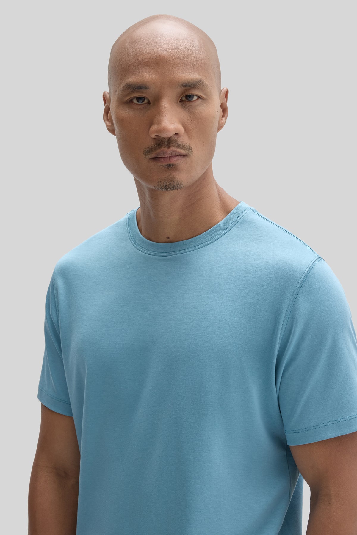 Man wearing light blue short-sleeve crewneck tee against neutral background.