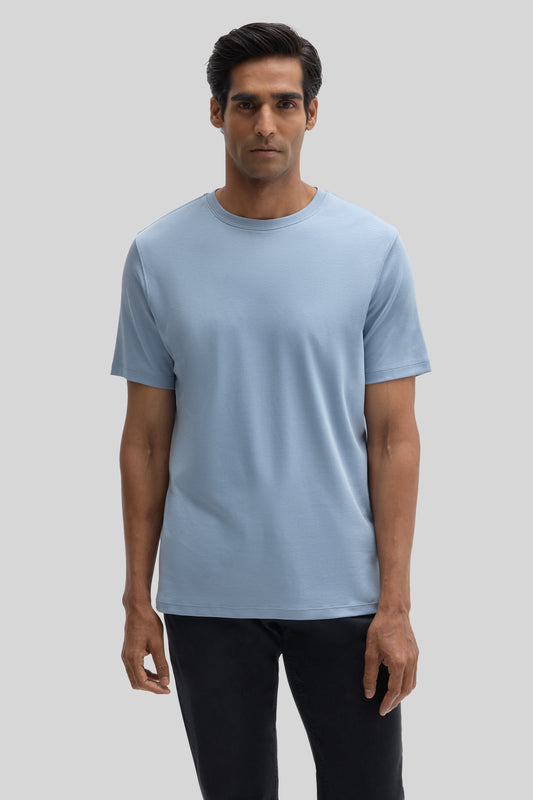 Man wearing light blue crewneck t-shirt with short sleeves and black pants against neutral background.
