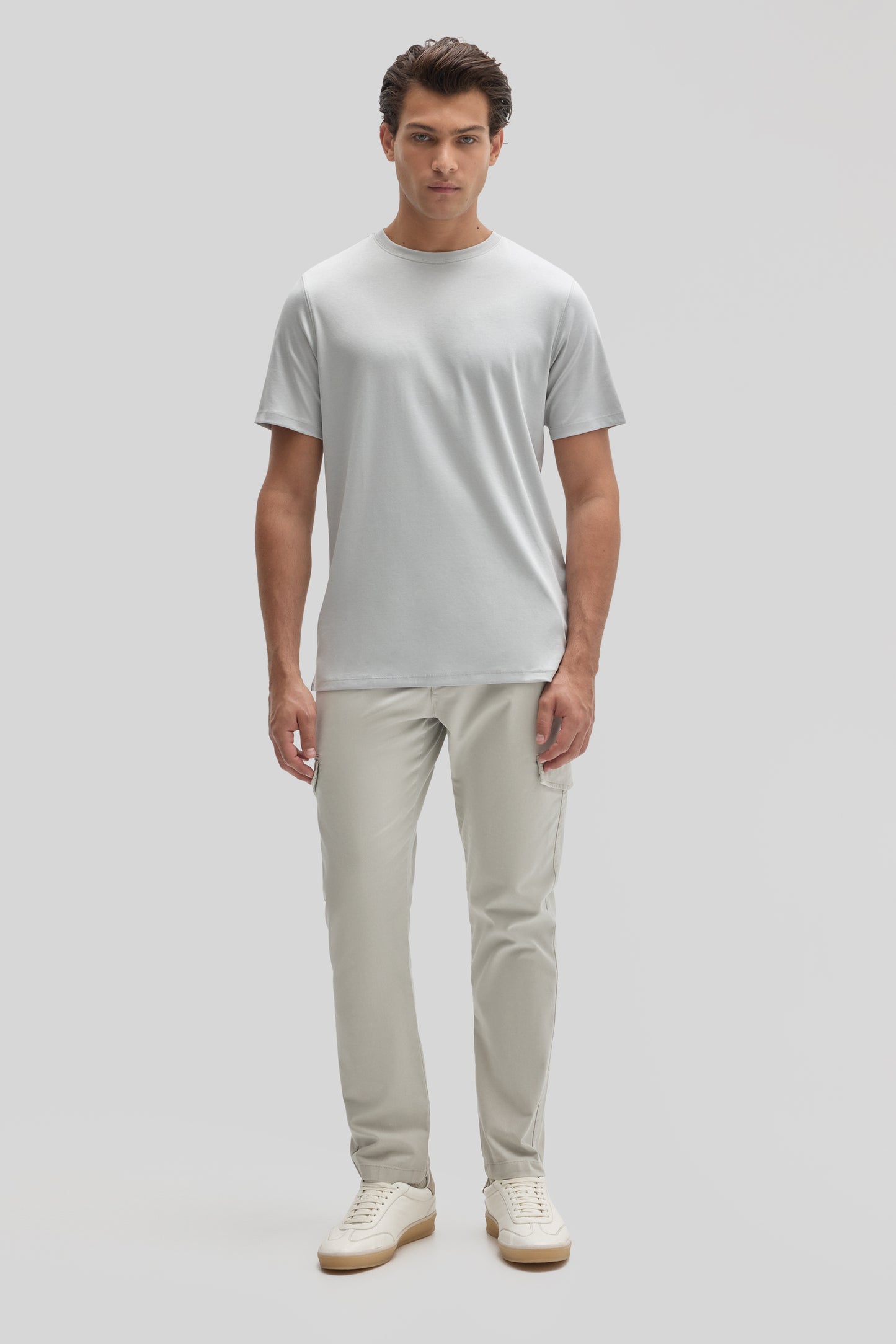 Man wearing light gray crew neck t-shirt with beige cargo pants and cream sneakers.