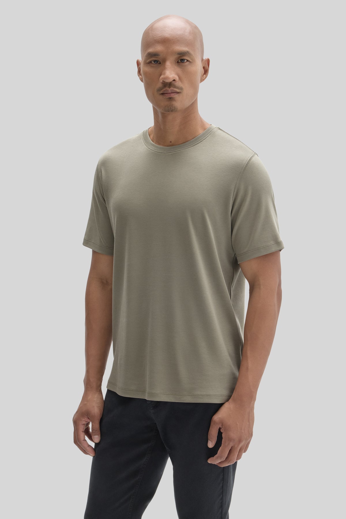 Man wearing a sage green crew neck t-shirt with short sleeves and black pants.