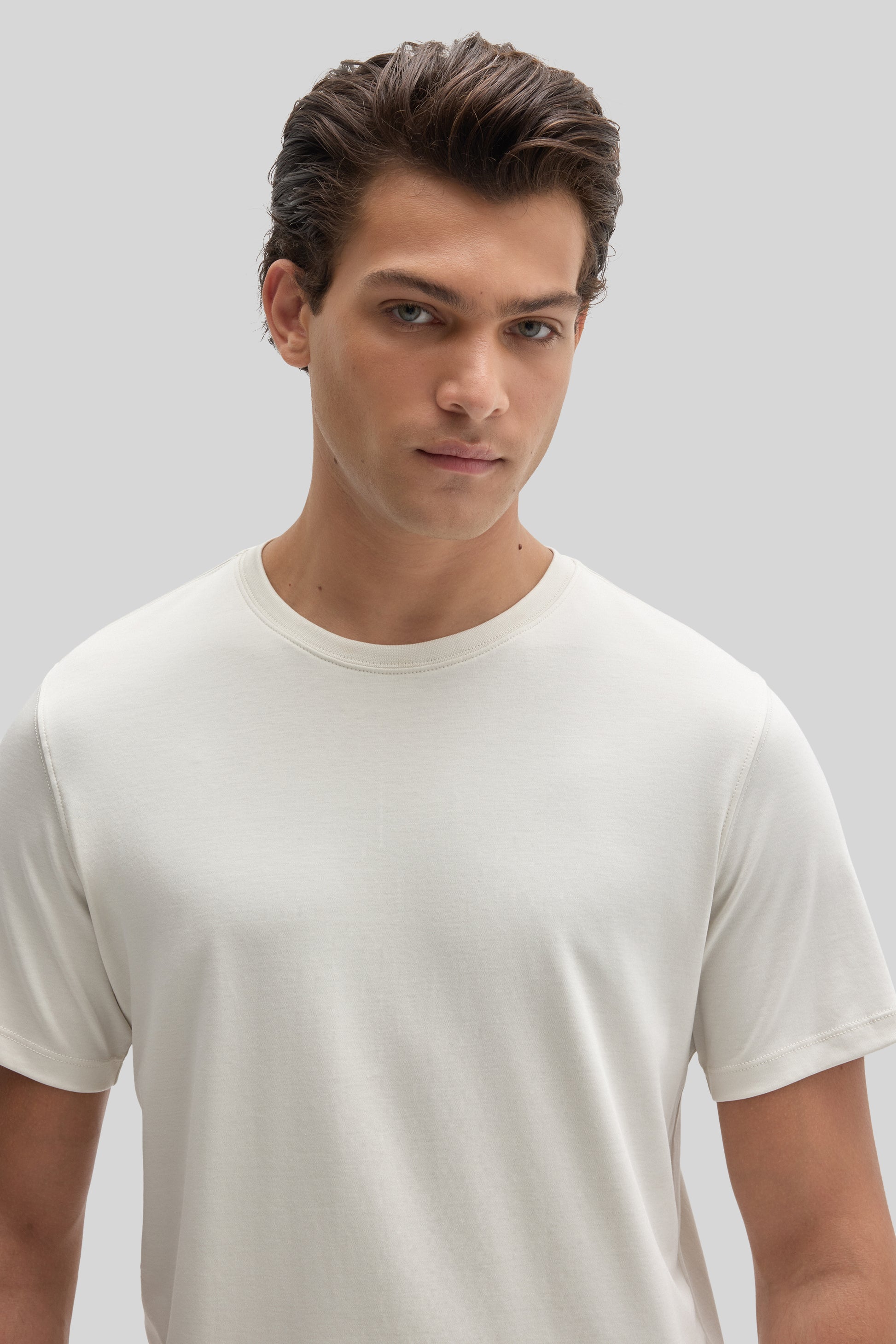 Man wearing a cream-colored crew neck t-shirt with short sleeves against a neutral background.