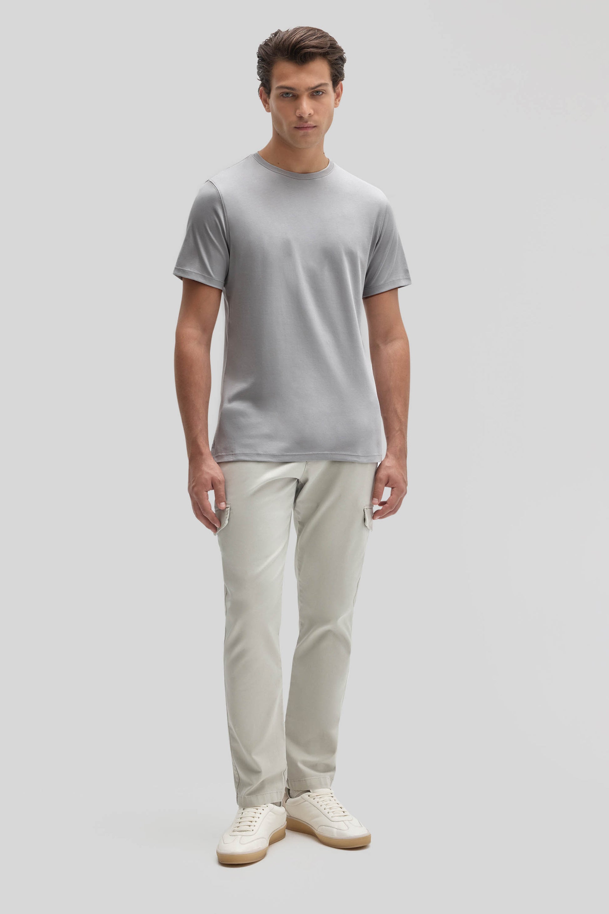 Man wearing a light gray crew neck t-shirt with short sleeves, paired with cream-colored pants and white sneakers.