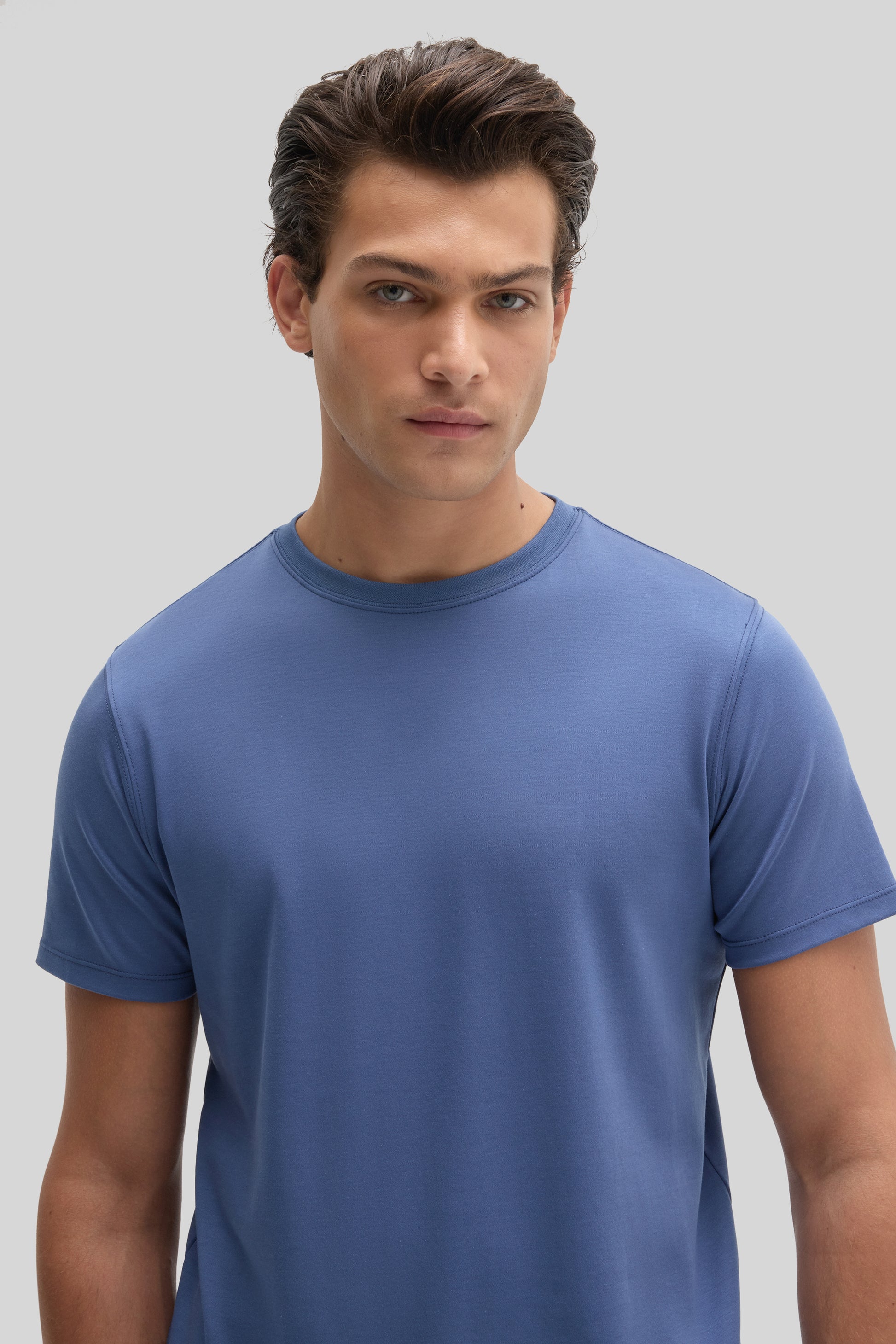 Man wearing a blue crew neck short-sleeve t-shirt against a neutral background.