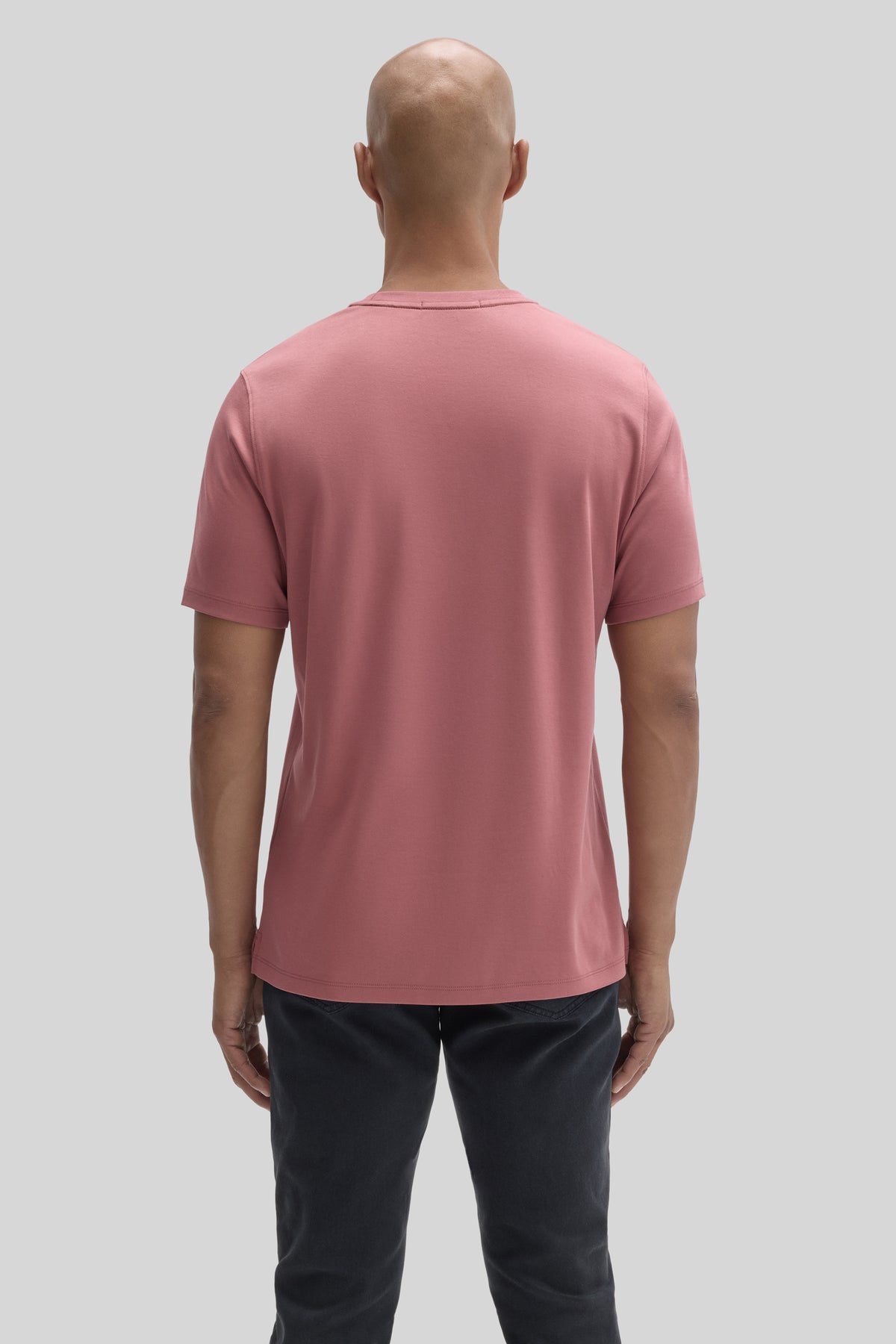 Man wearing a pink short-sleeve t-shirt and dark pants, shown from behind.