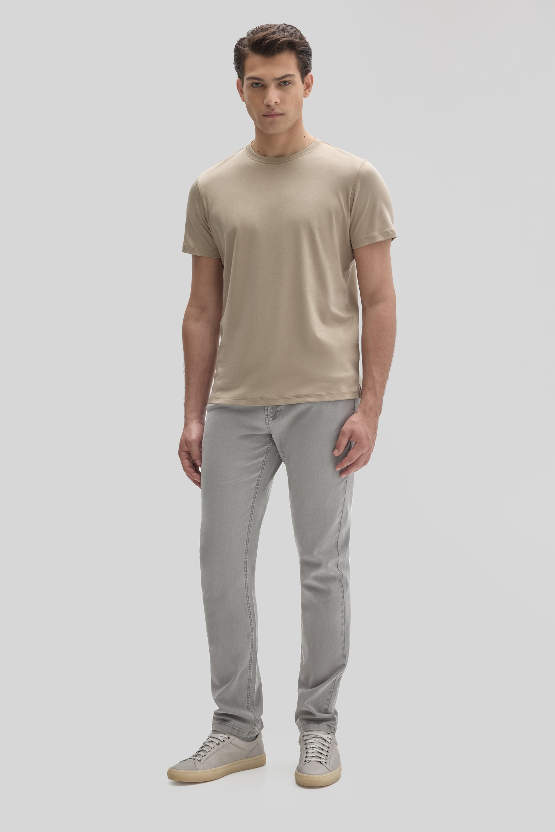 Man wearing a beige crew neck t-shirt with short sleeves, gray jeans, and light gray sneakers.