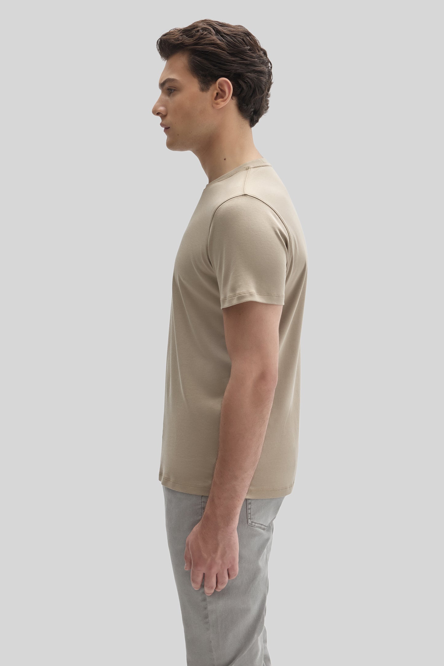 Man wearing a beige crewneck short-sleeve t-shirt with gray jeans, shown in side profile.