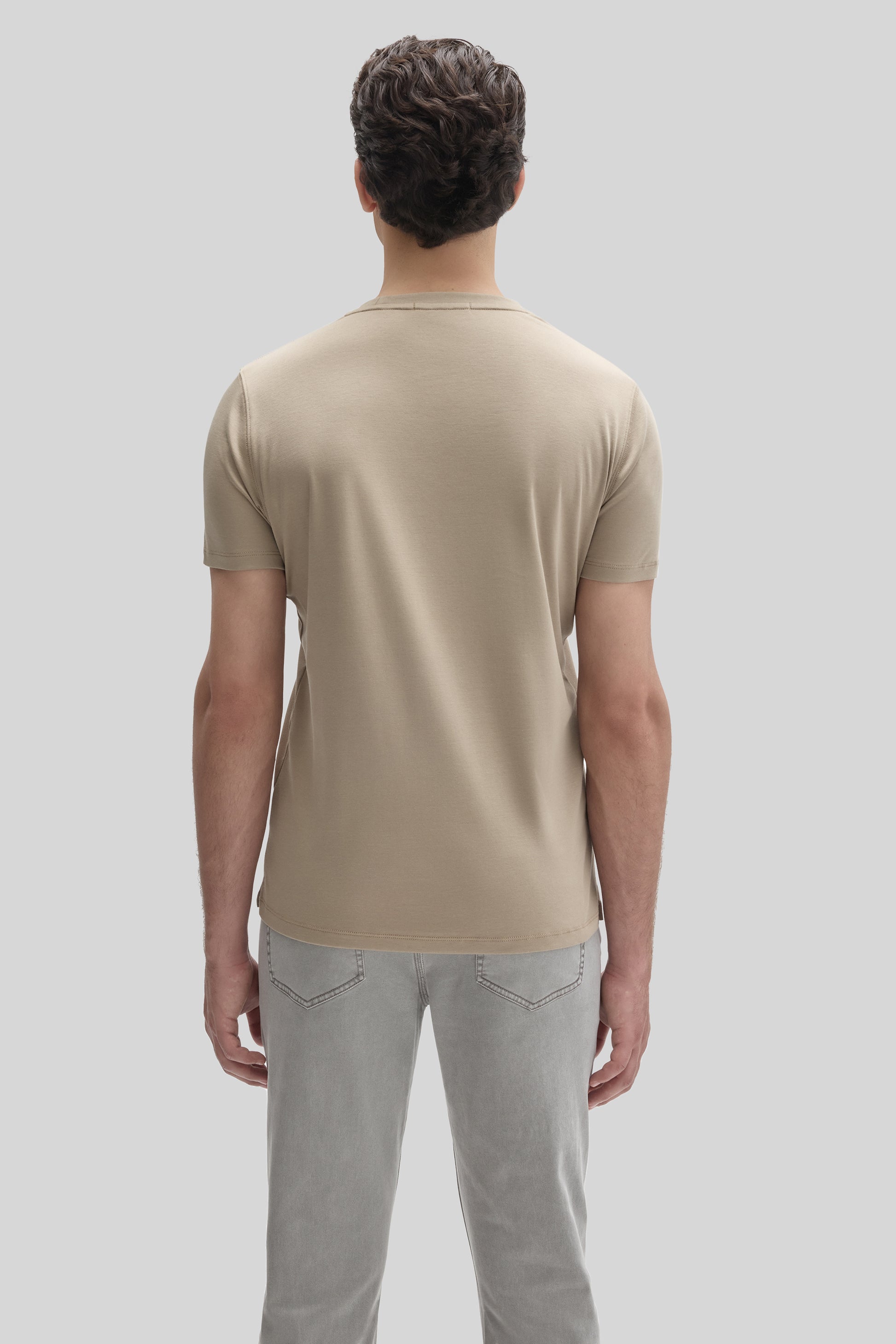 Man wearing a beige short-sleeve t-shirt and light gray jeans, shown from the back.
