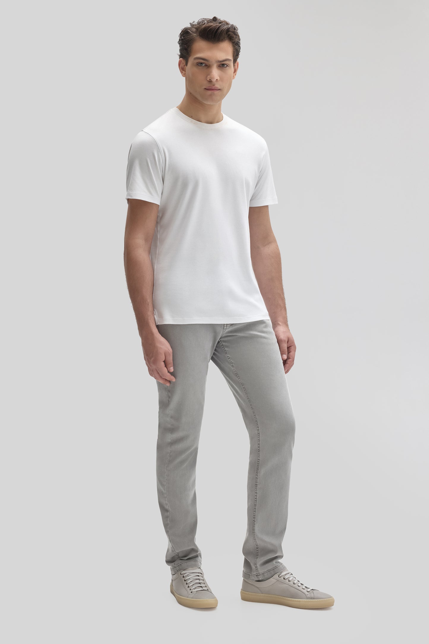 Man wearing white crew neck short-sleeve t-shirt with gray jeans and beige canvas sneakers.