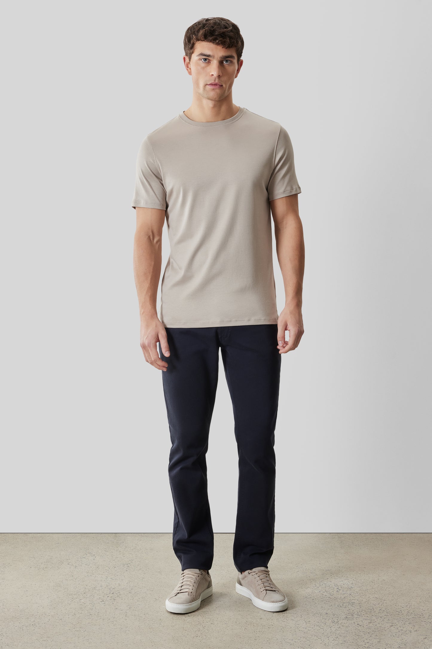 Man wearing beige crew neck t-shirt with short sleeves and dark navy pants.
