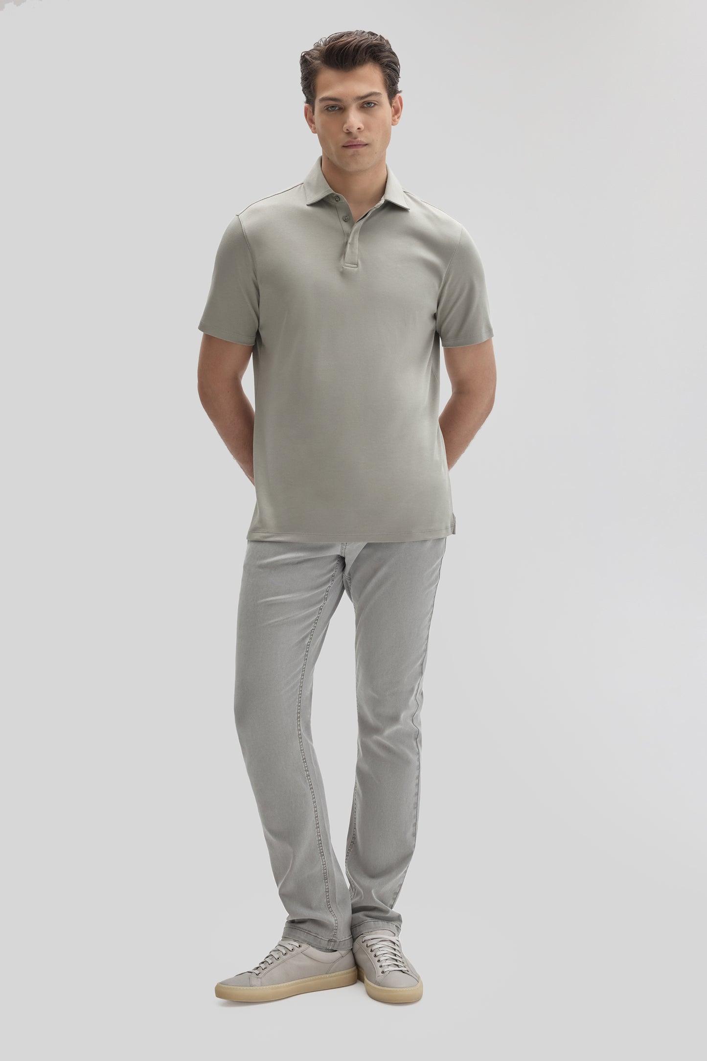 Man wearing light gray short-sleeve polo shirt with covered placket and matching gray jeans with sneakers.
