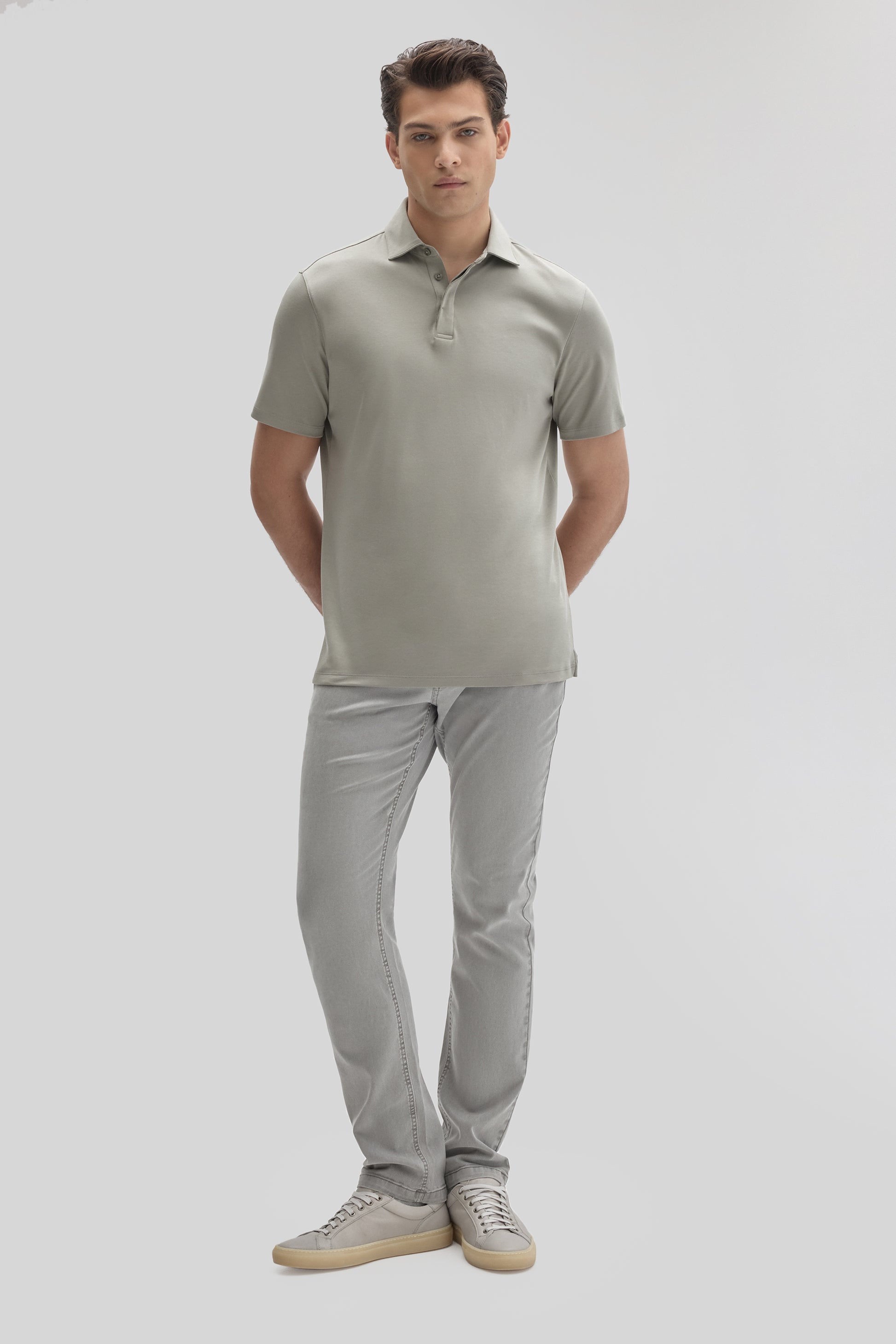 Man wearing light gray short-sleeve polo shirt with covered placket and matching gray jeans with sneakers.