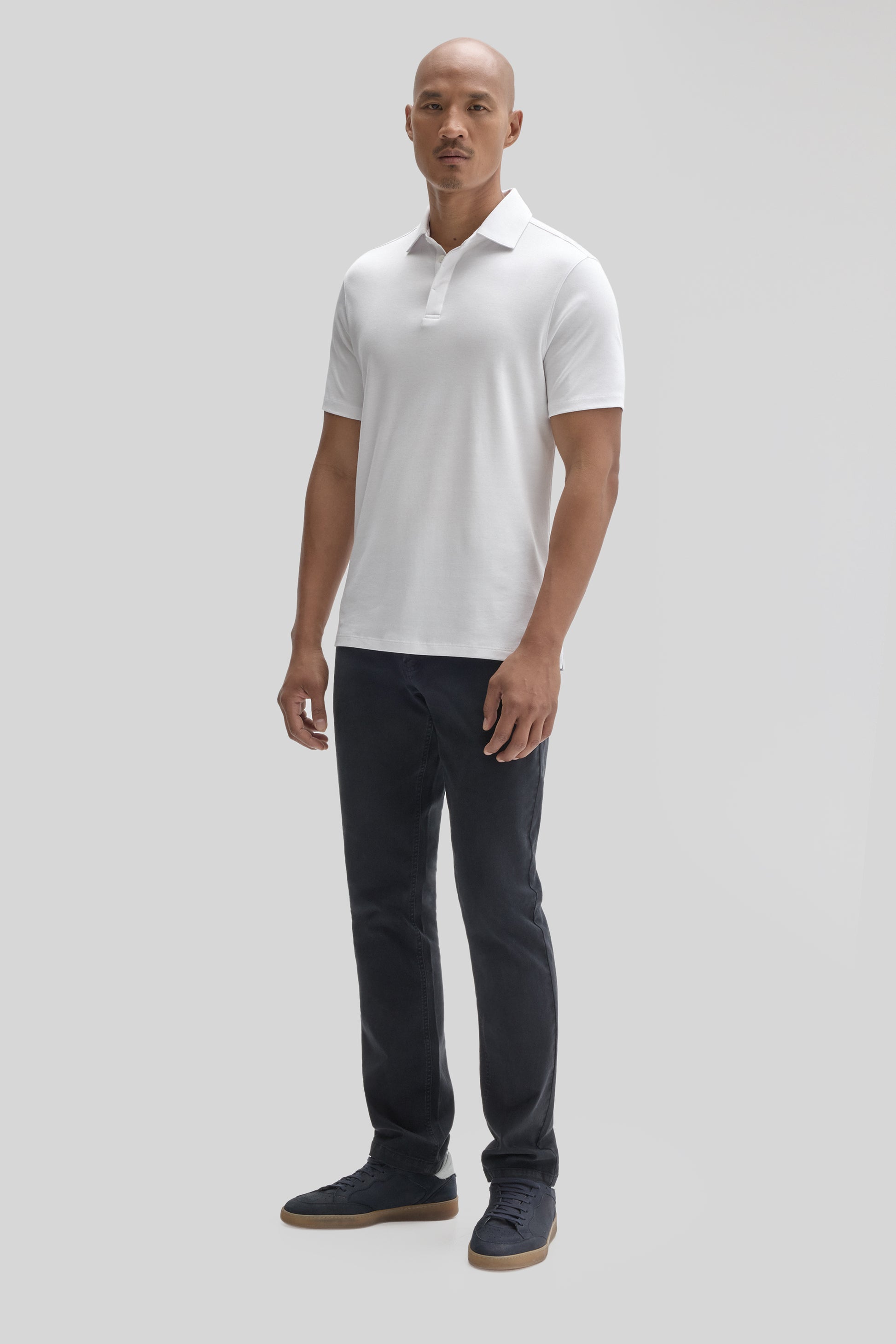 Man wearing white short-sleeve polo shirt with covered placket and dark jeans.