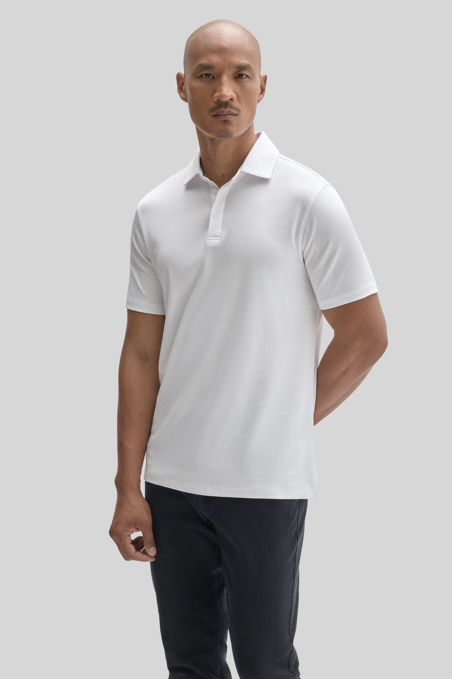 Man wearing white short-sleeve polo shirt with covered placket and collar, paired with dark pants.