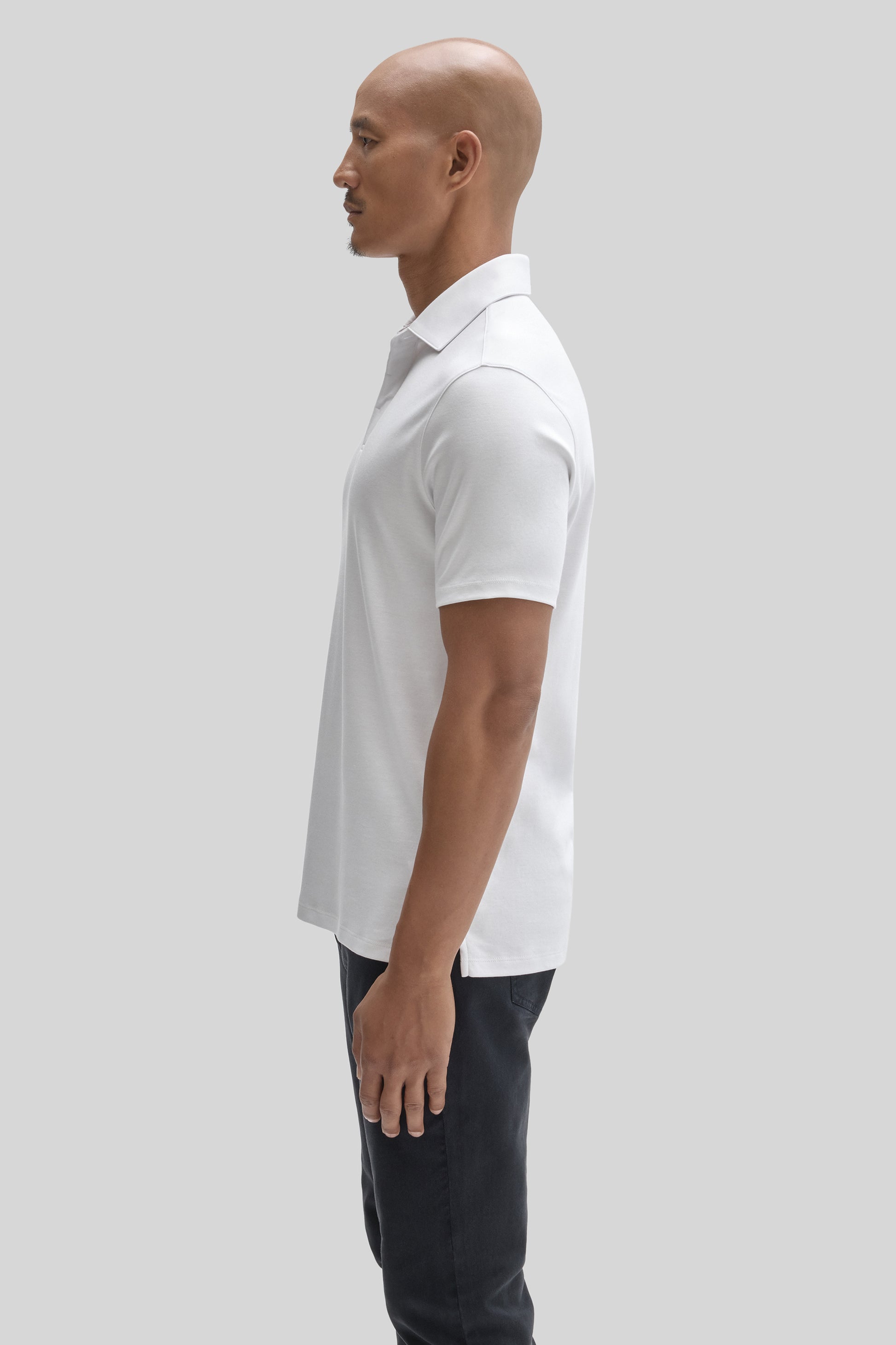 Man wearing white short-sleeve polo shirt with covered placket and dark trousers, shown in profile view.