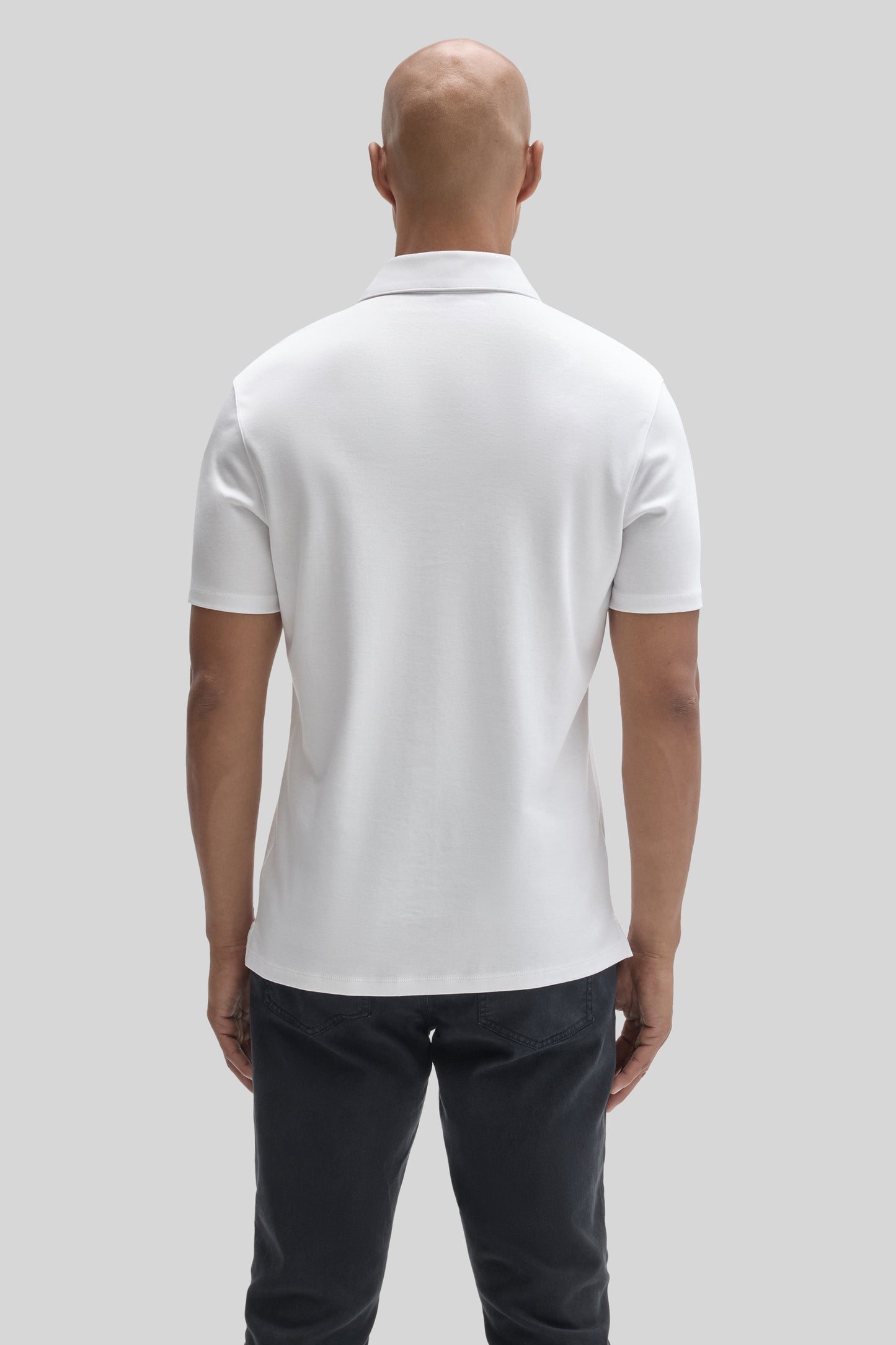 Man wearing white short-sleeve polo shirt with collar, shown from back, paired with dark jeans.
