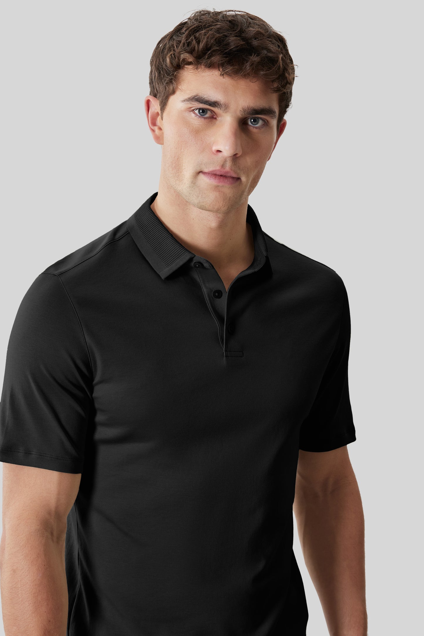Black short-sleeve polo shirt with textured collar and button placket, worn by man against neutral background.
