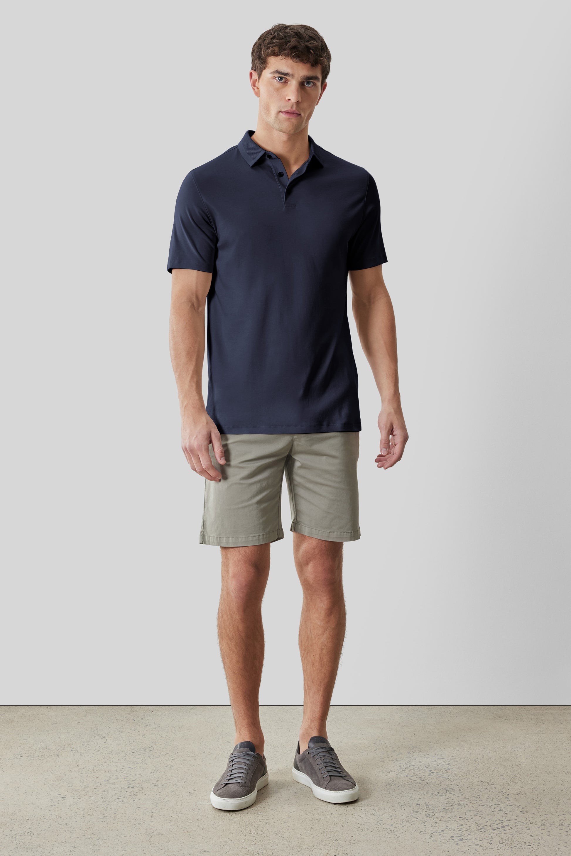 Man wearing navy short-sleeve polo shirt with textured collar and beige shorts.
