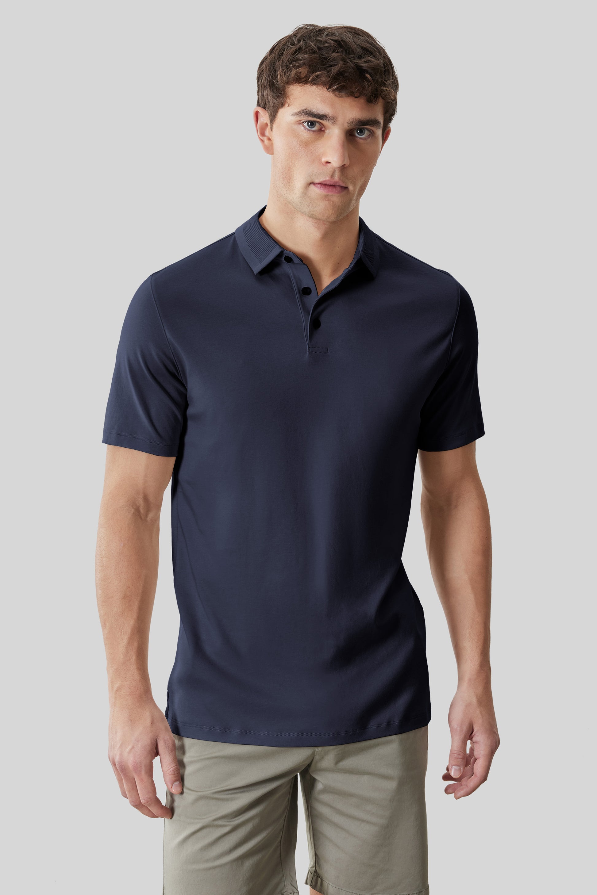 Man wearing navy short-sleeve polo shirt with textured collar and button placket, paired with beige pants.