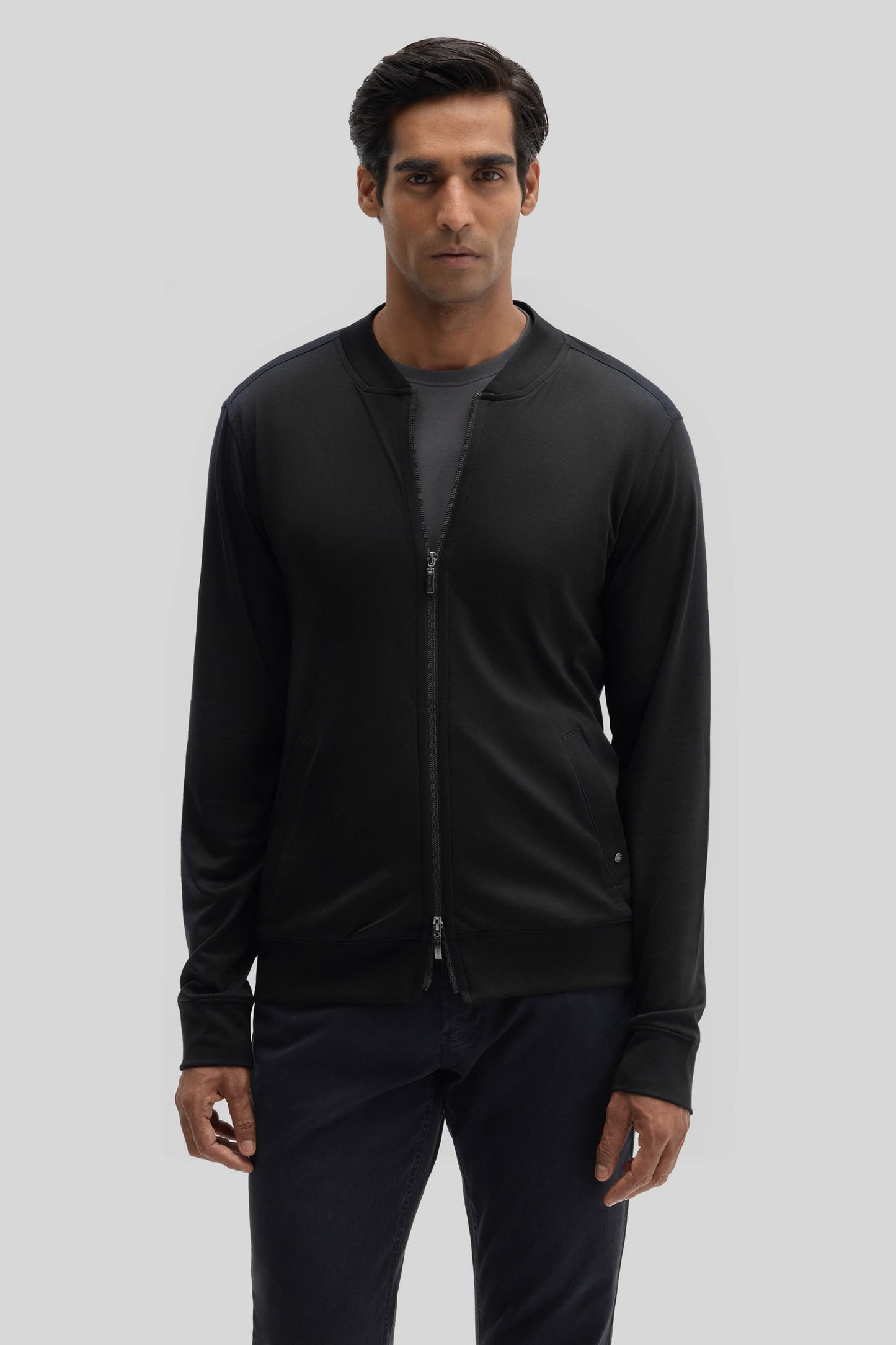 Man wearing black baseball jacket with full-length zip and ribbed cuffs over dark pants.