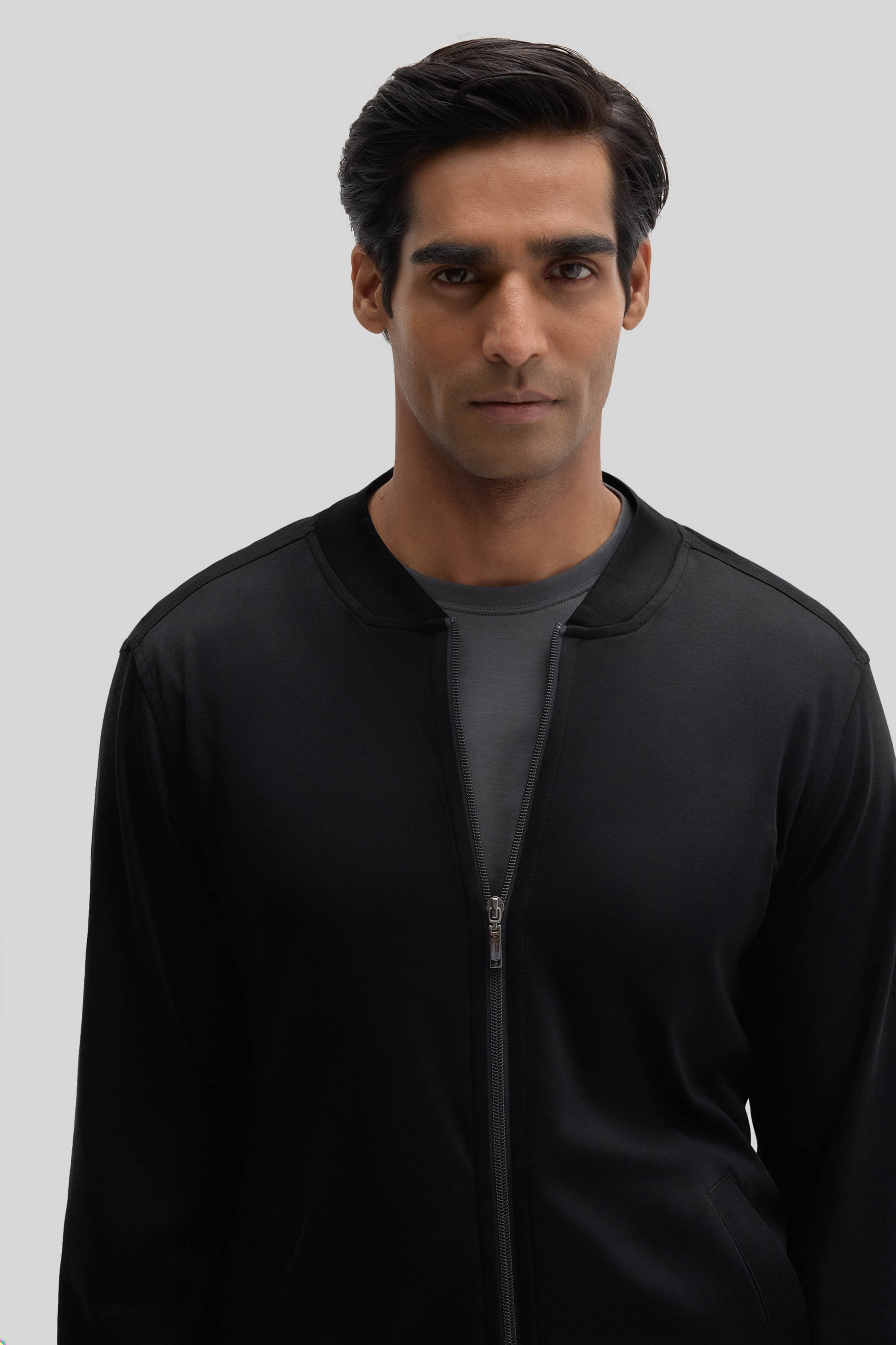 Black baseball jacket with full-length zipper and ribbed collar worn by man against neutral background.
