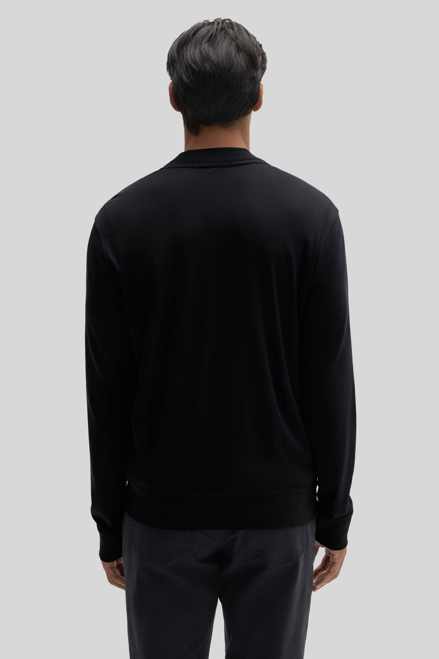 Black baseball jacket with collar and ribbed cuffs, shown from back view on model wearing dark pants.