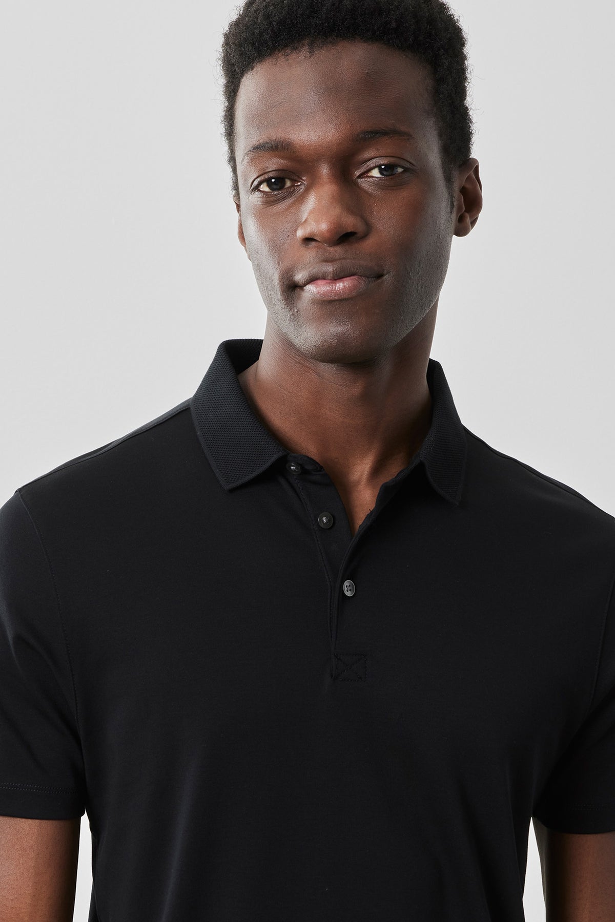 Black polo shirt with button front closure and textured collar, worn by a man against a neutral background.