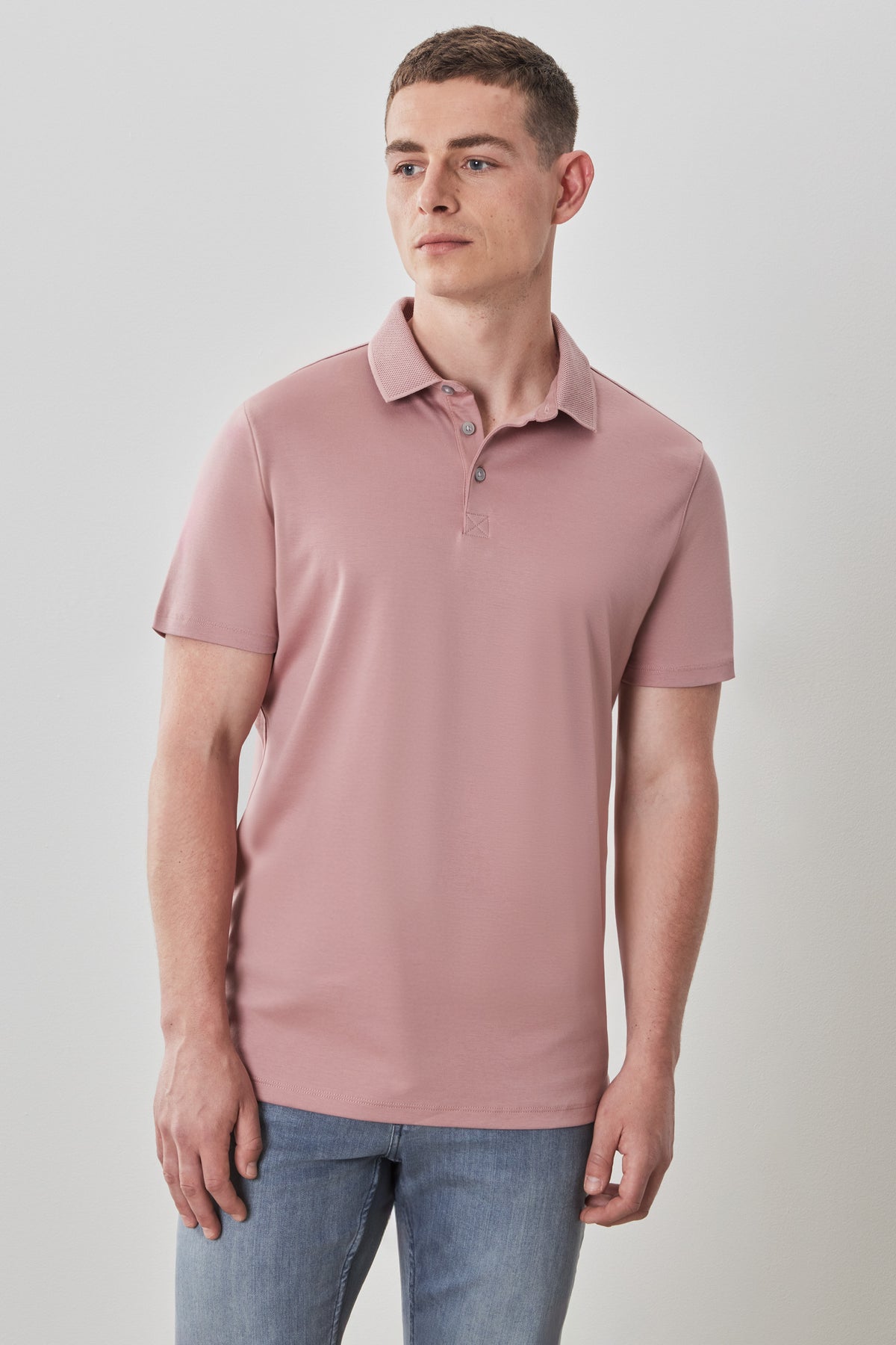Man wearing a dusty pink short-sleeve polo shirt with button placket and collar, paired with blue jeans.
