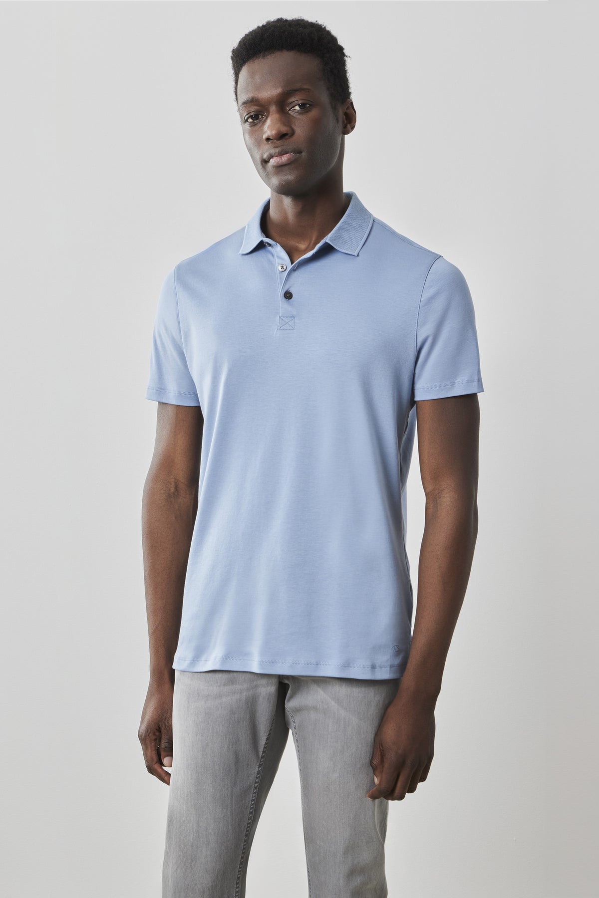 Man wearing light blue short-sleeve polo shirt with collar and button placket, paired with gray pants.