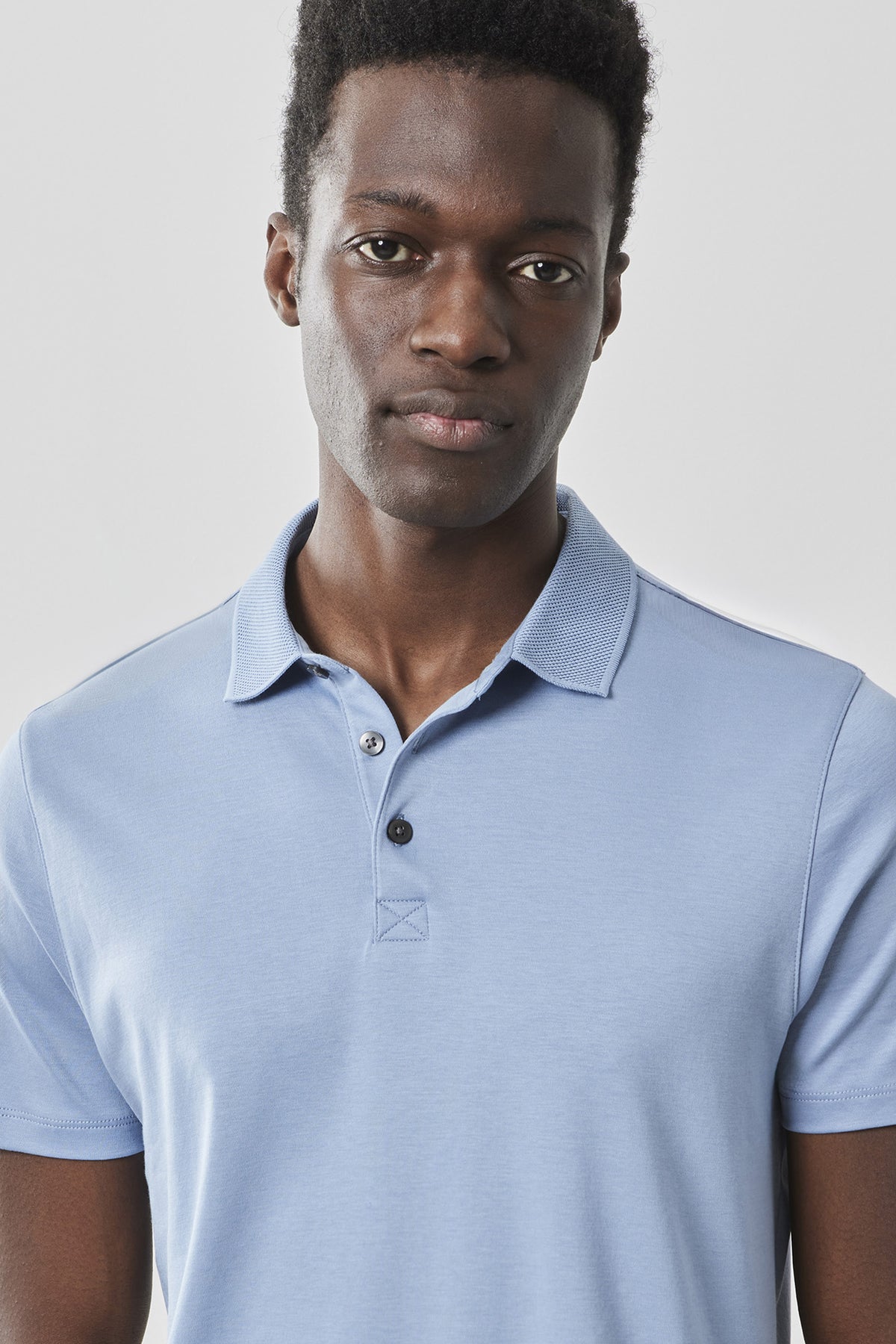 Man wearing light blue polo shirt with short sleeves and button placket.