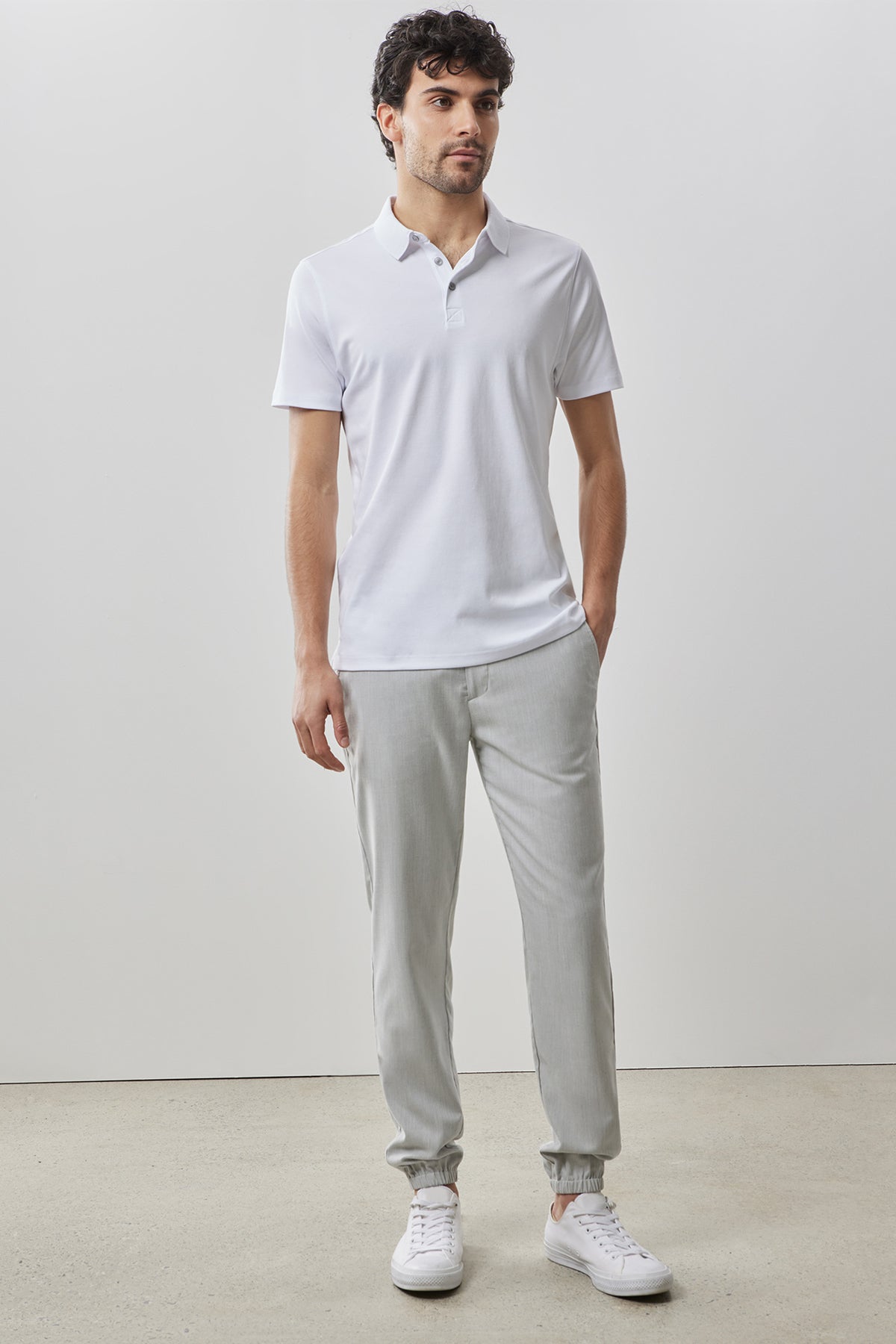 Man wearing white short-sleeve polo shirt with collar and light gray tapered pants, paired with white sneakers.