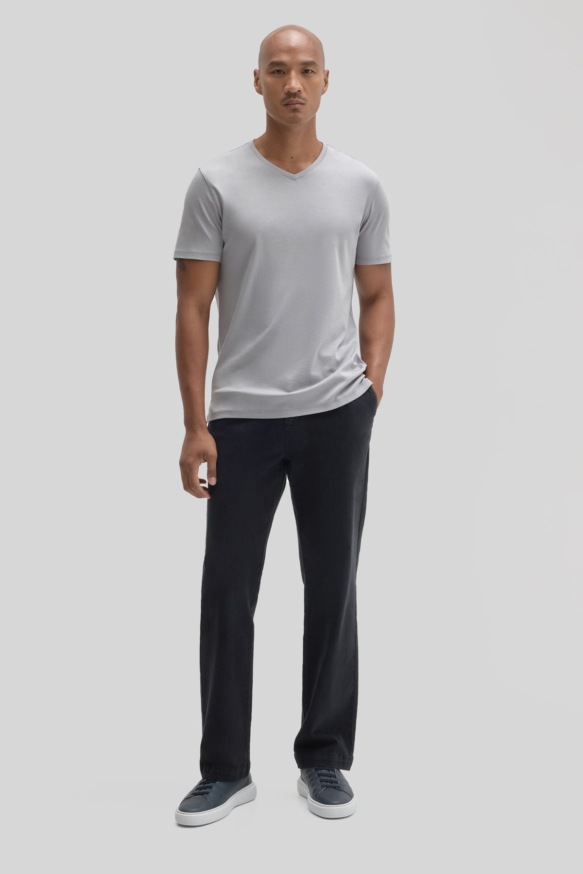 Man wearing light gray V-neck short-sleeve tee with black pants and navy sneakers.