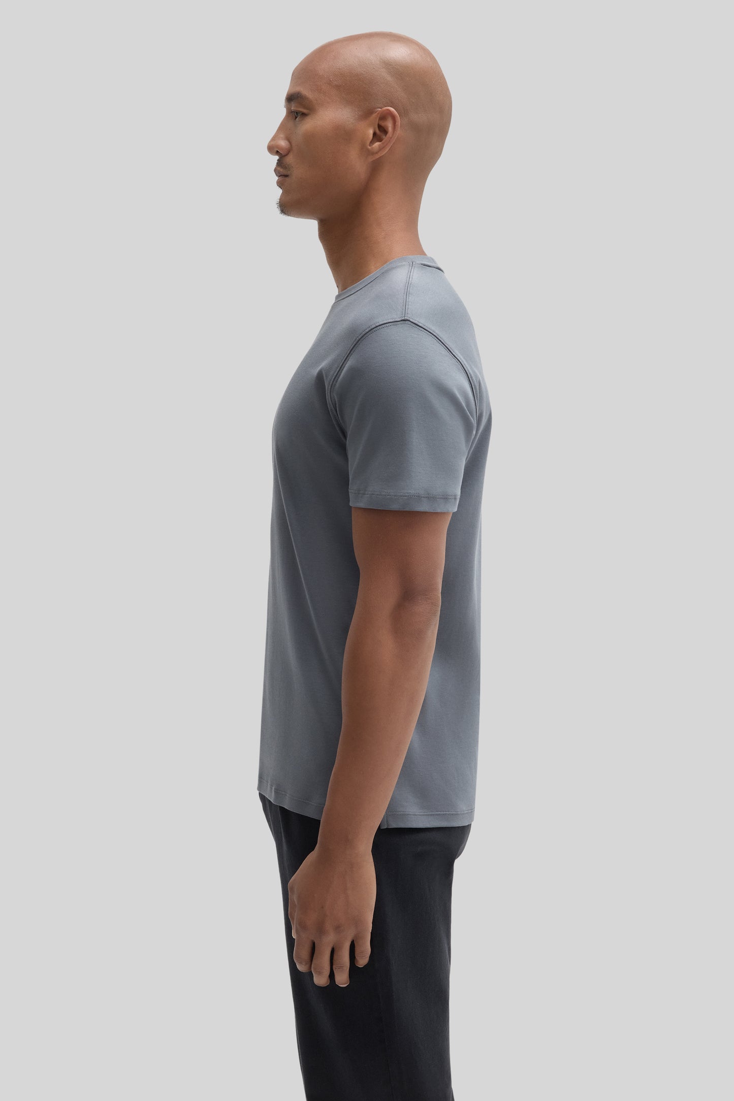 Man wearing a slate blue short-sleeve t-shirt with black pants, shown in profile view.