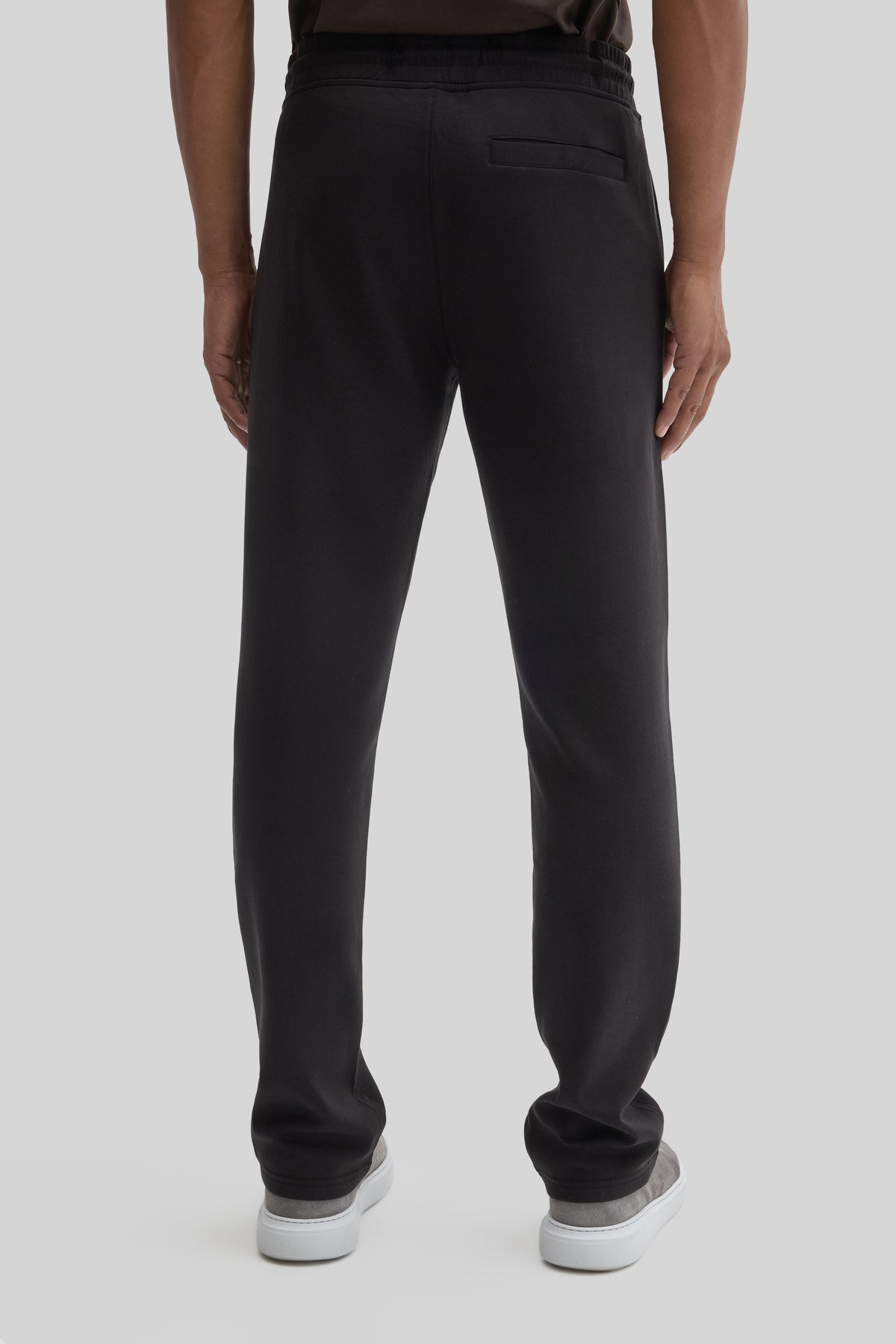 Black jogging pants with elastic waistband and cuffs, back pocket visible, worn with white sneakers.
