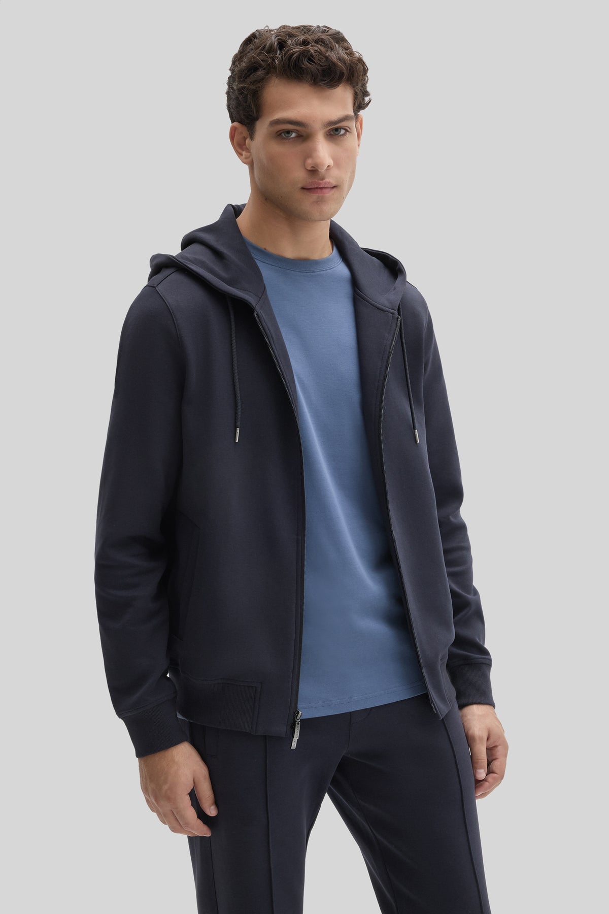 Man wearing dark navy full zip hoodie with drawstring hood and kangaroo pocket over blue t-shirt.