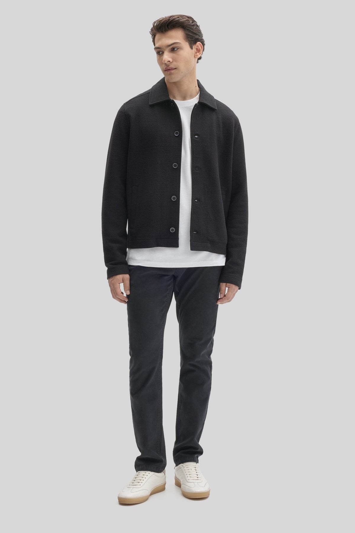 Black buttoned jacket with textured fabric and collar, worn over white t-shirt with dark pants.
