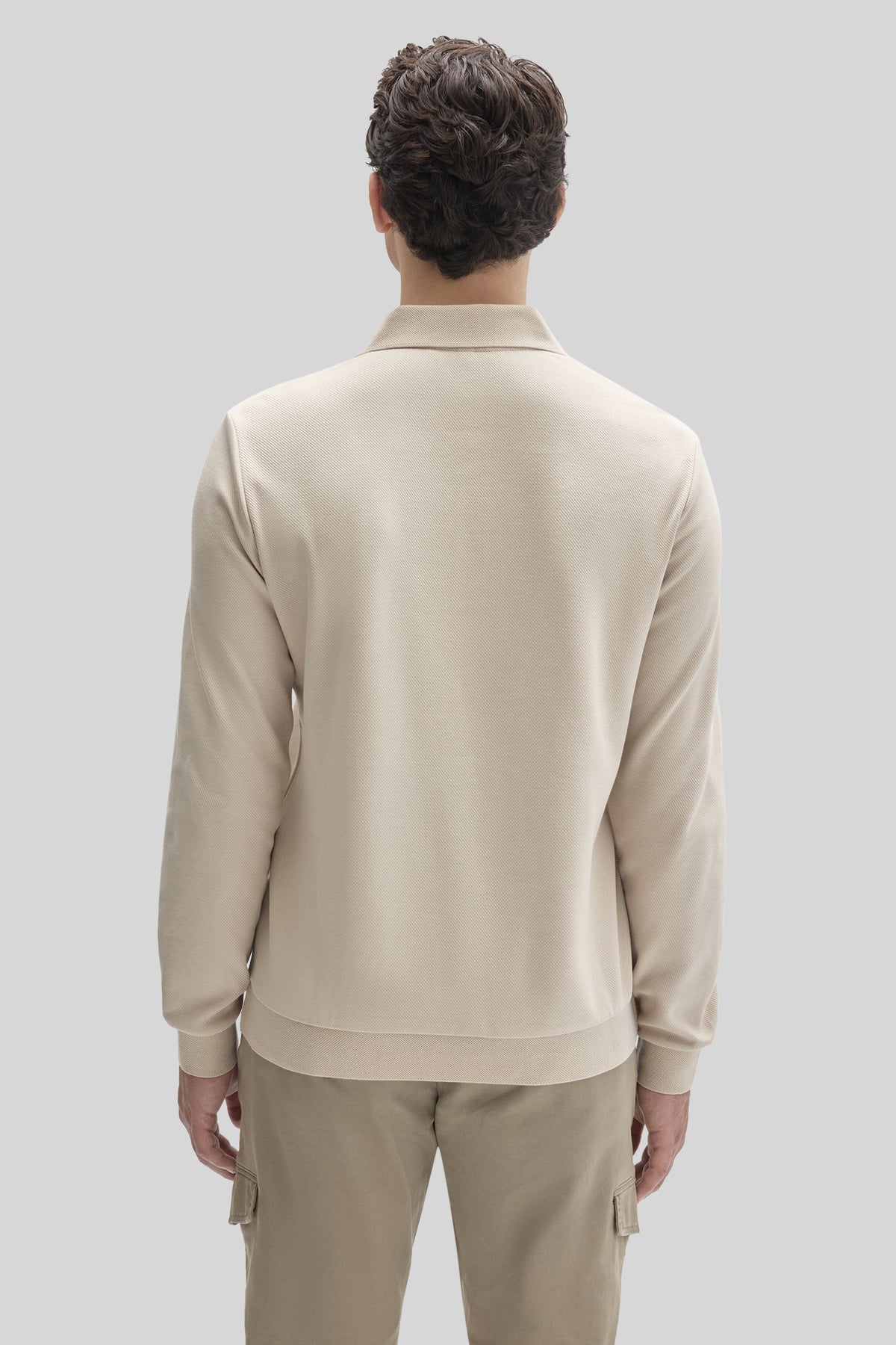Man wearing cream long sleeve polo shirt with collar, shown from back view.
