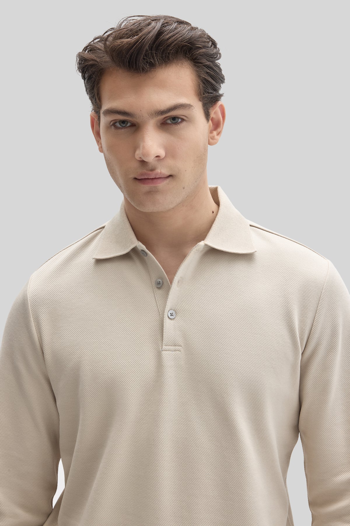 Man wearing cream long sleeve polo shirt with textured fabric and button placket.