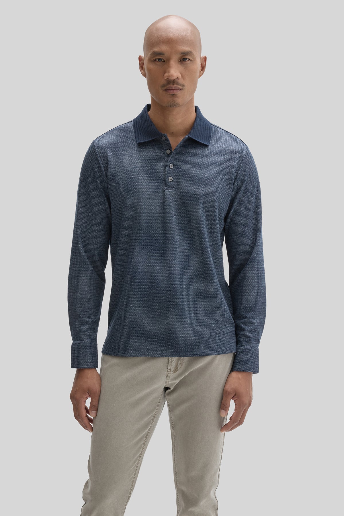 Man wearing a navy blue long sleeve polo shirt with button placket and beige pants.