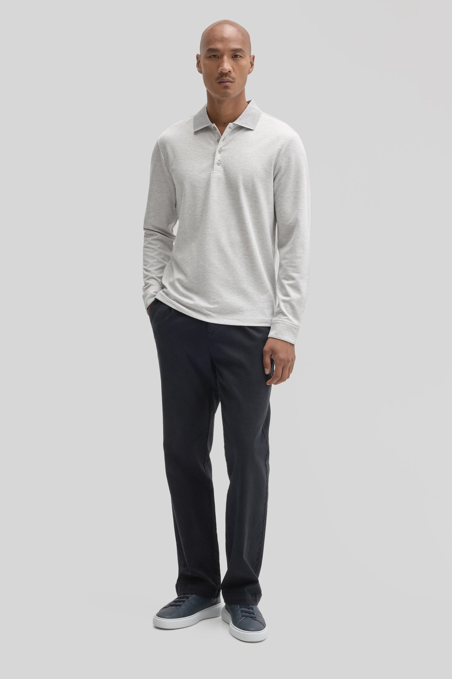 Man wearing light gray long sleeve polo shirt with collar and button placket, paired with dark navy trousers and navy sneaker