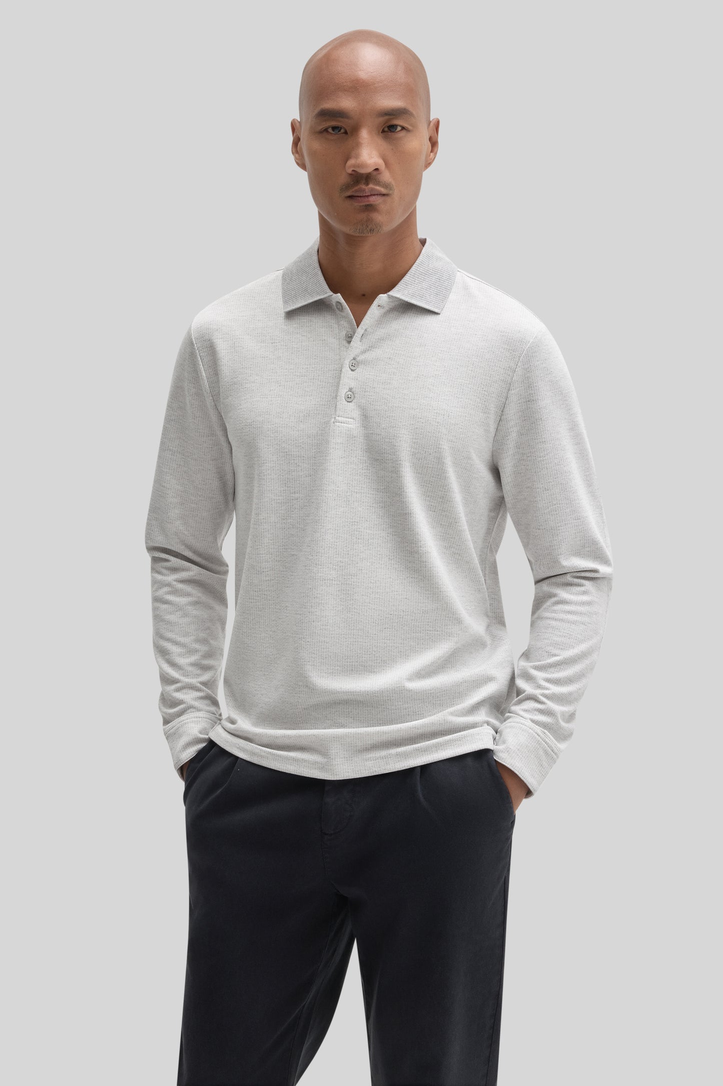 Man wearing light gray long sleeve polo shirt with collar and button placket, paired with dark navy pants.