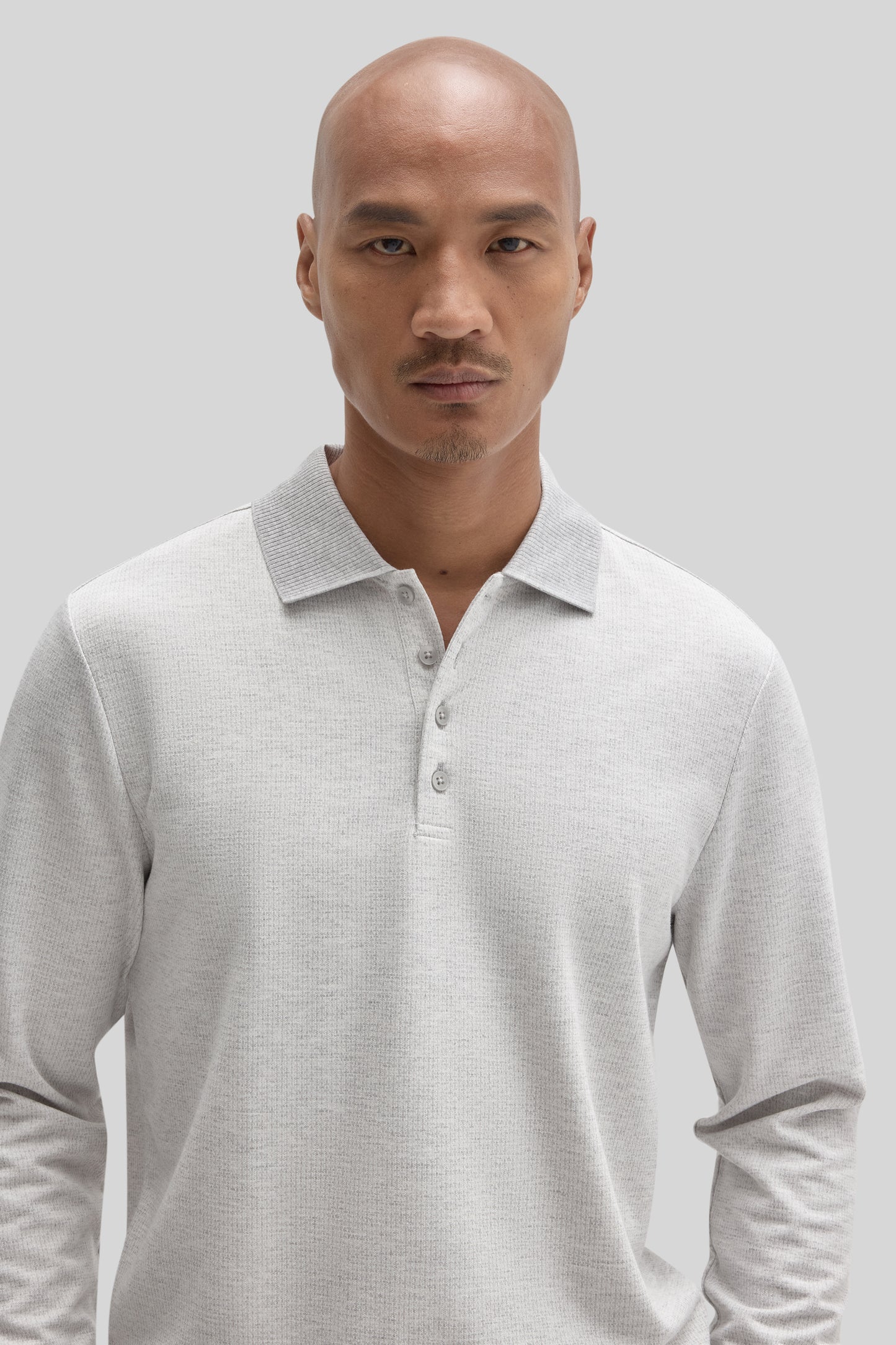 Man wearing a light gray long sleeve polo shirt with a textured knit fabric and button placket.