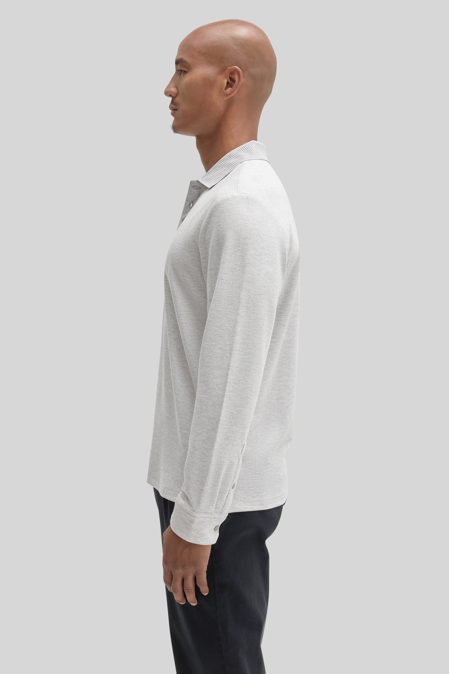 Man wearing white long sleeve polo with textured fabric and collared neckline, paired with black pants.