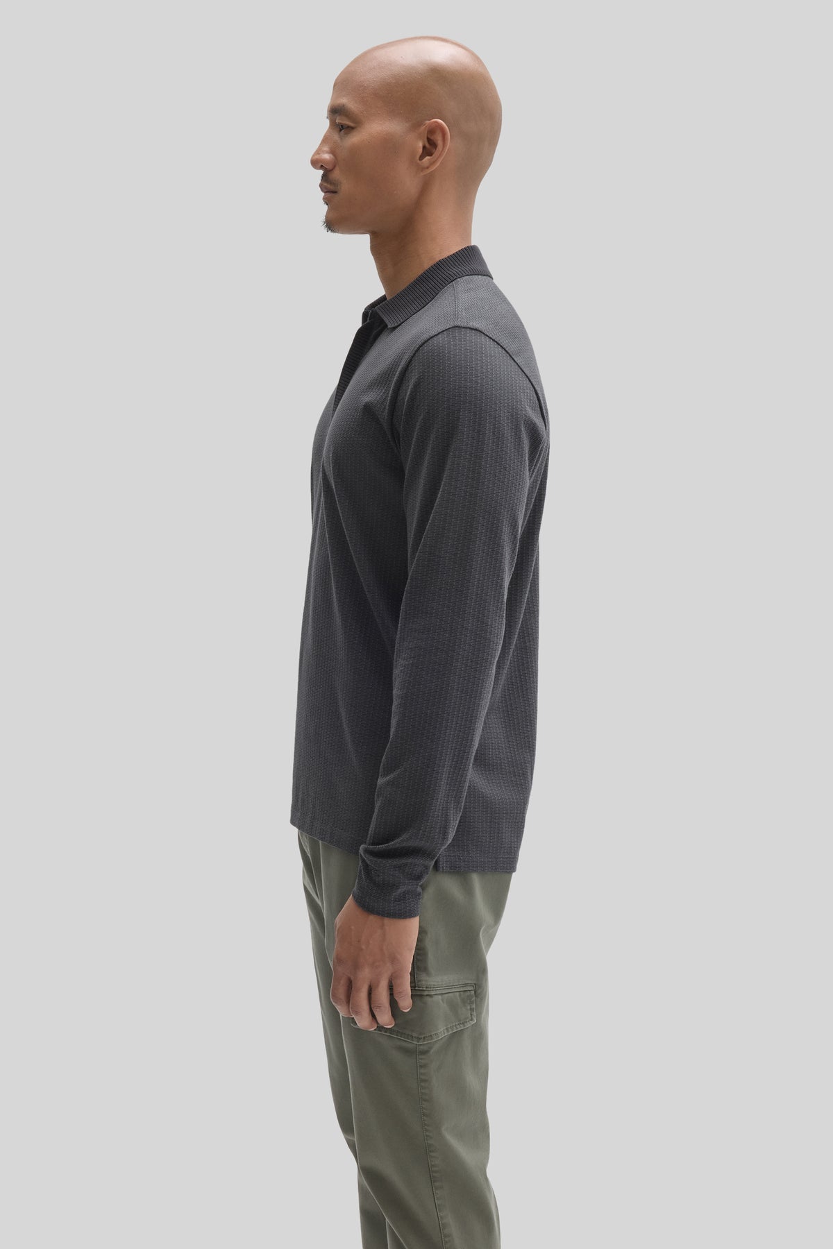 Man wearing dark gray long-sleeve polo with ribbed collar and placket zip, paired with olive green pants.