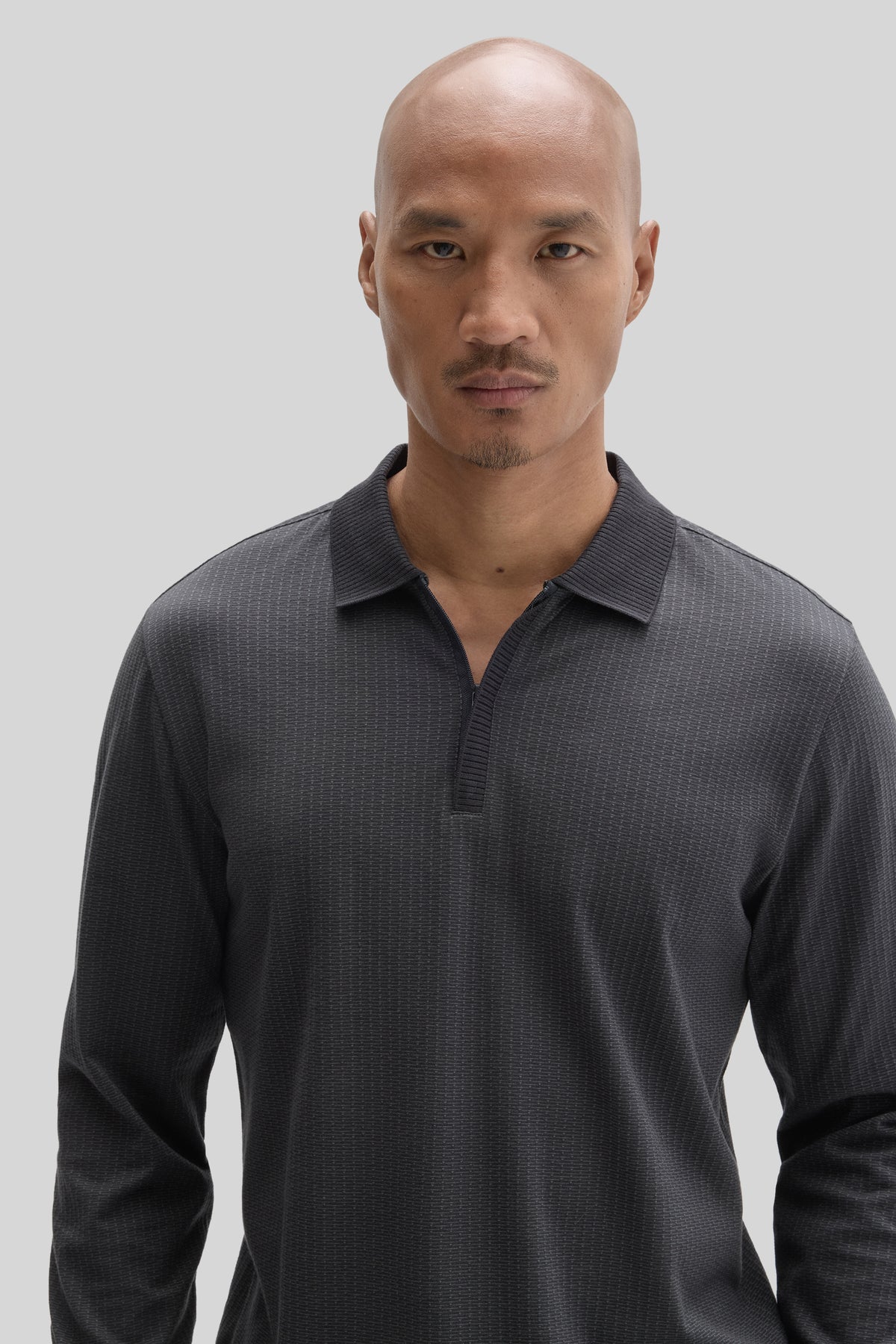 Man wearing charcoal long-sleeve polo shirt with placket zip and subtle textured pattern.