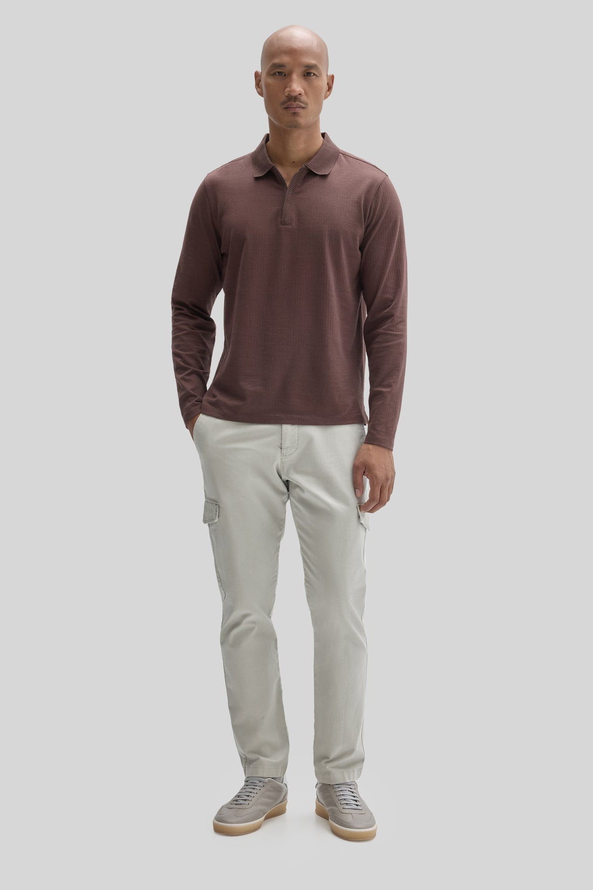 Man wearing brown long-sleeve polo shirt with collar and placket, paired with beige cargo pants and gray sneakers.